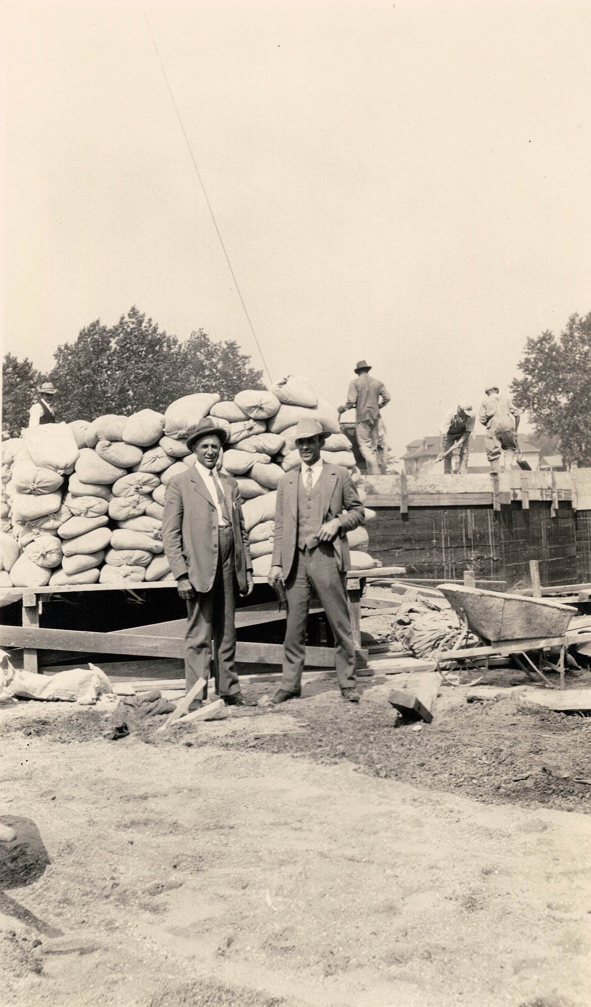 Two men are standing in front of a pile of bags.
