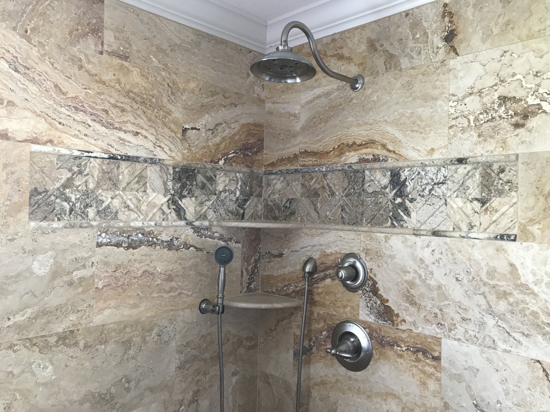 Corner shower with tan stone walls, silver fixtures, and decorative center tile band.