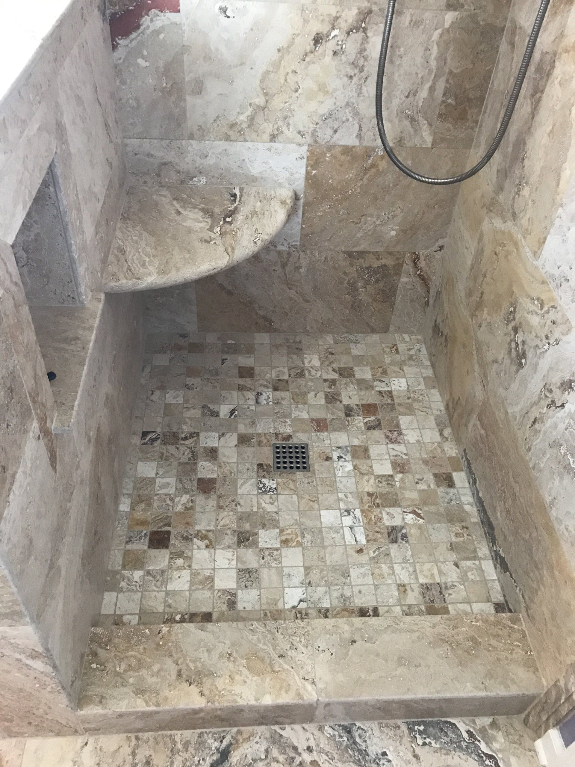Stone-tiled shower stall with built-in bench, drain in the center, and showerhead at the top.