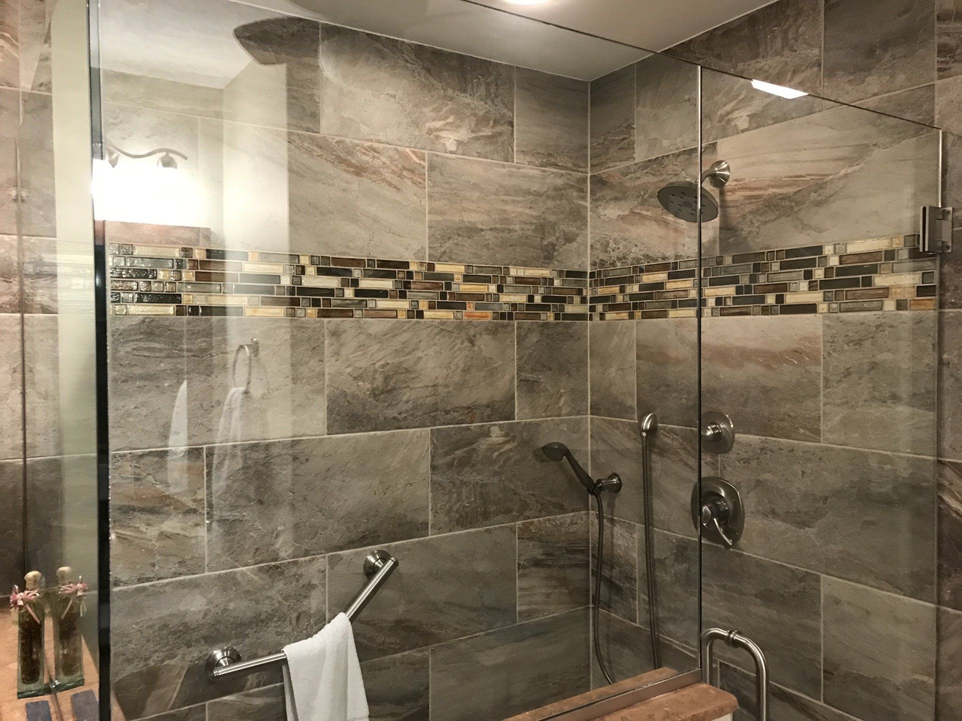 Modern shower with gray stone tiles, glass doors, and brown accent strip.