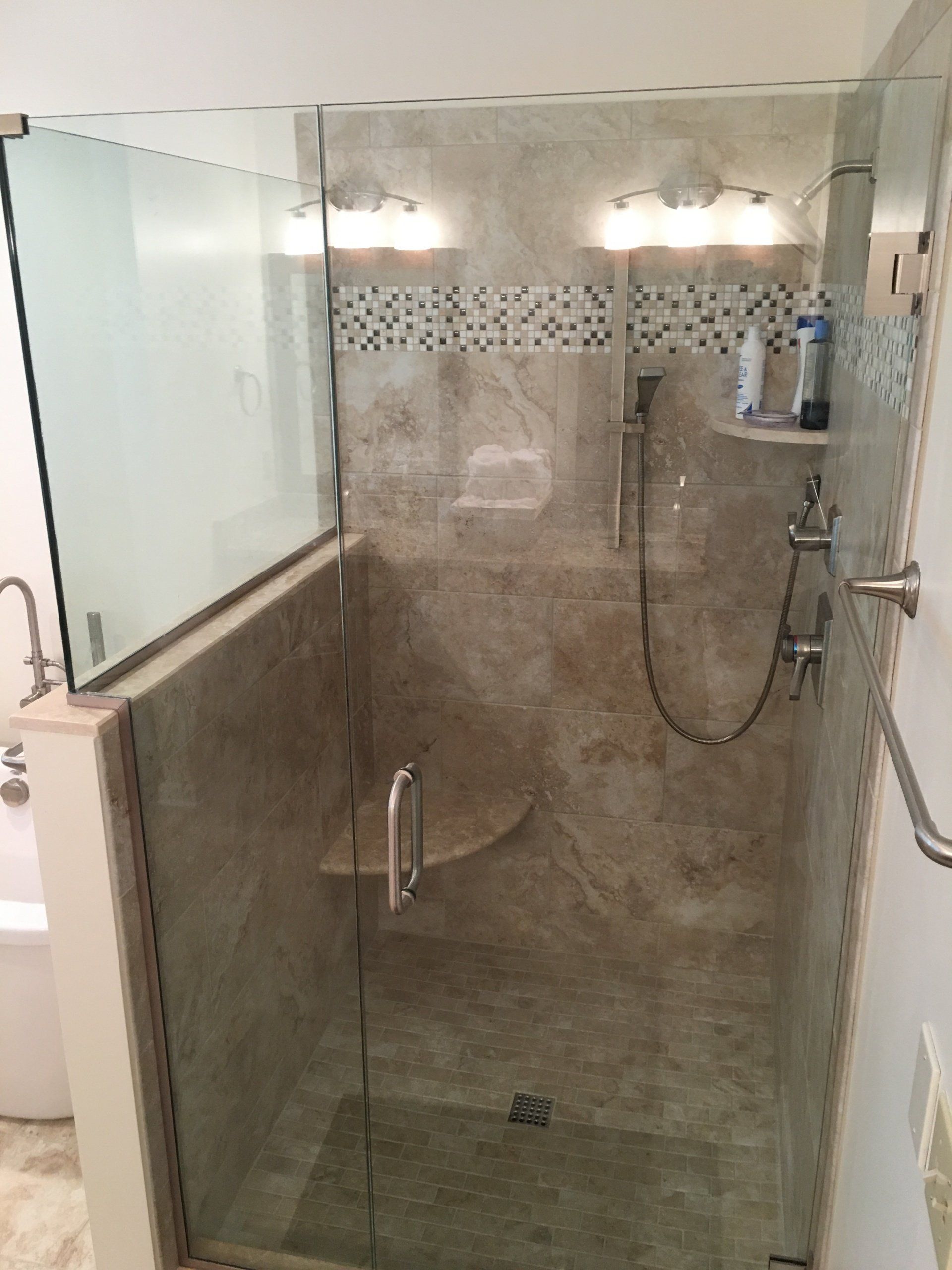 A shower enclosure with glass doors and a built-in bench; light tile walls.