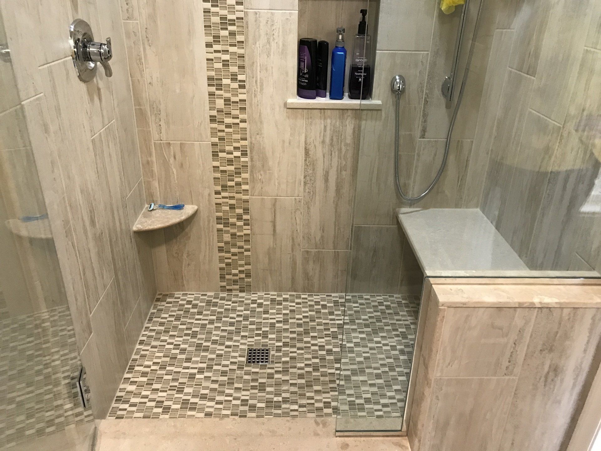 Shower with light-colored tile walls, mosaic tile floor, built-in bench, and shampoo niche.