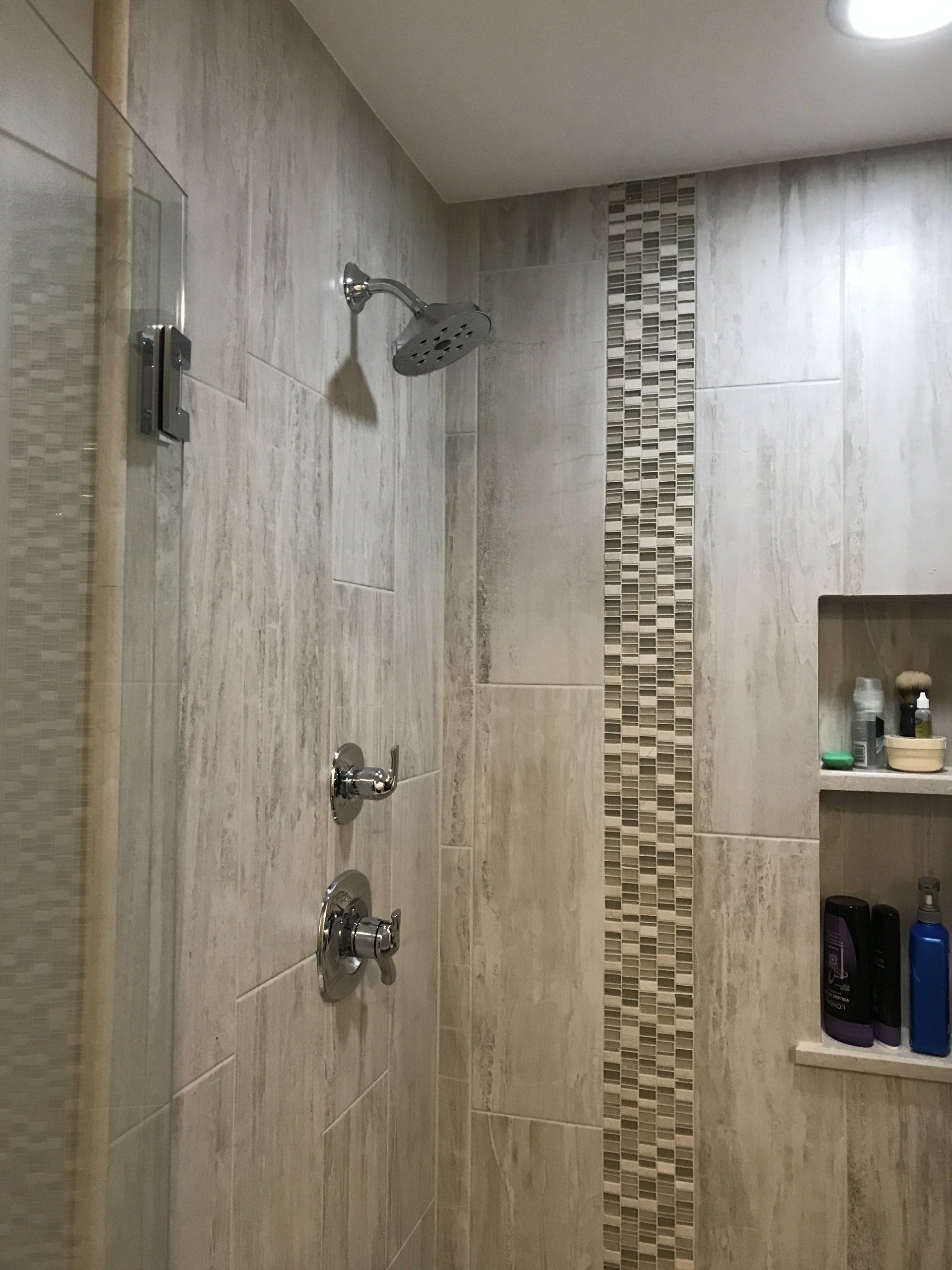 Bathroom with light-colored tiled walls, showerhead, and a decorative mosaic strip.