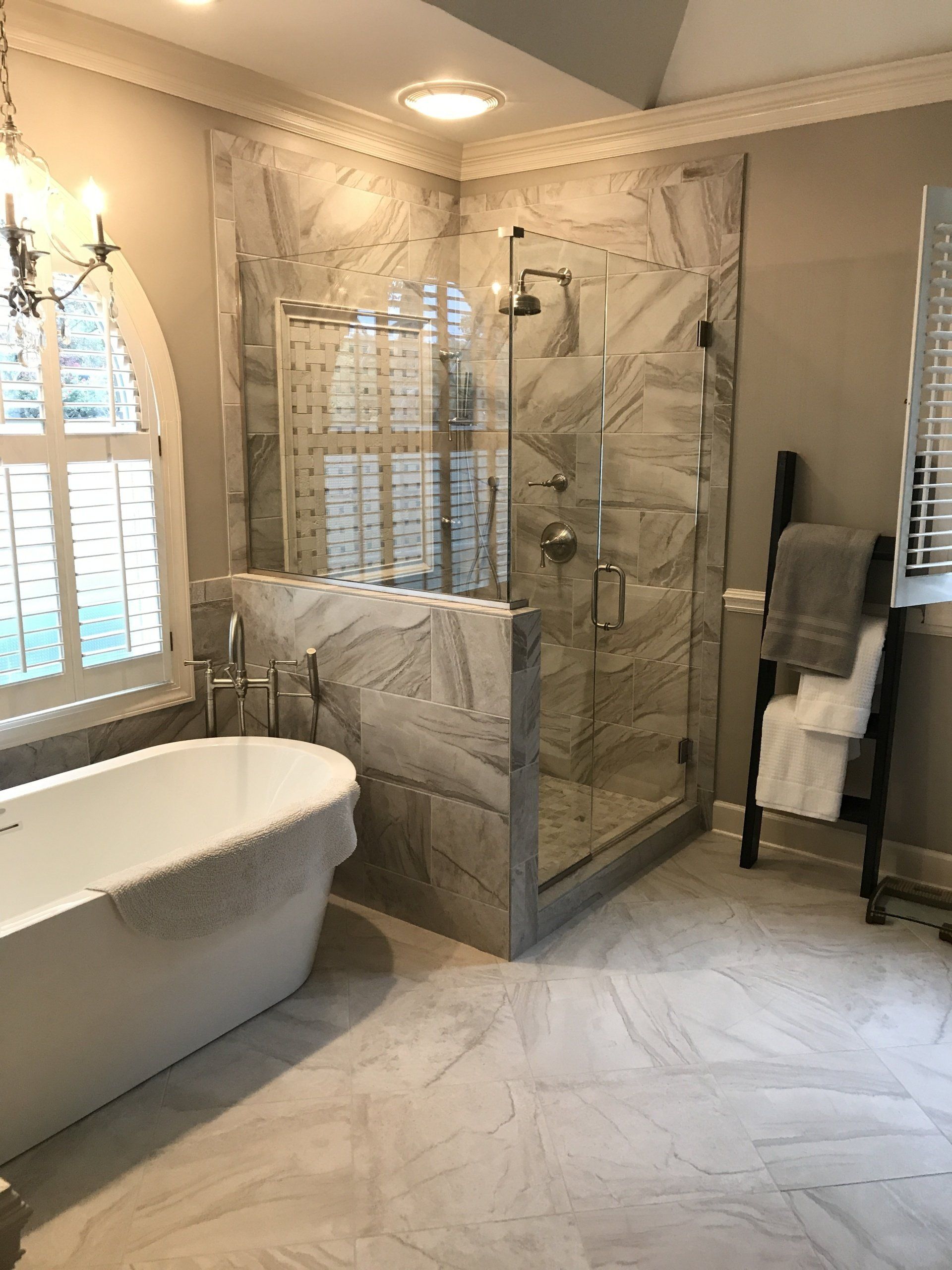 Elegant bathroom with marble shower and bathtub, next to a shuttered window and towel ladder.