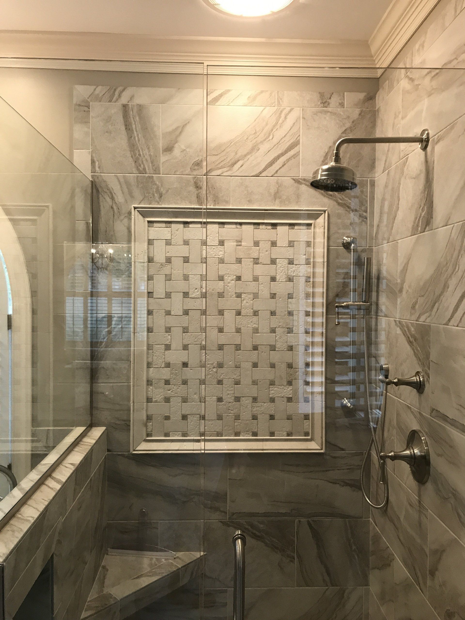 Marble shower with glass door, built-in basket-weave niche, and silver fixtures.