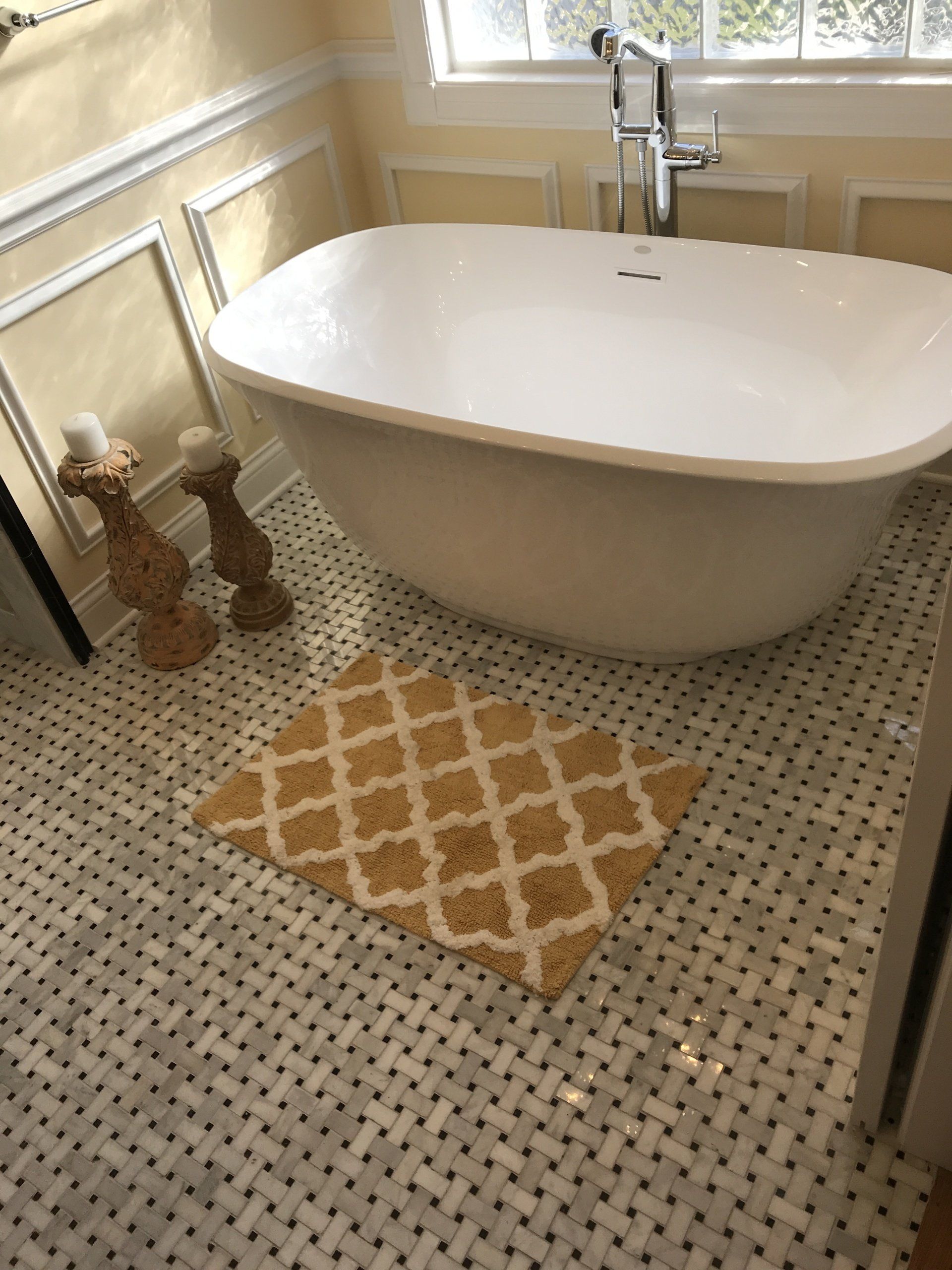 Bathroom with white tub, yellow rug, and marble tile floor.
