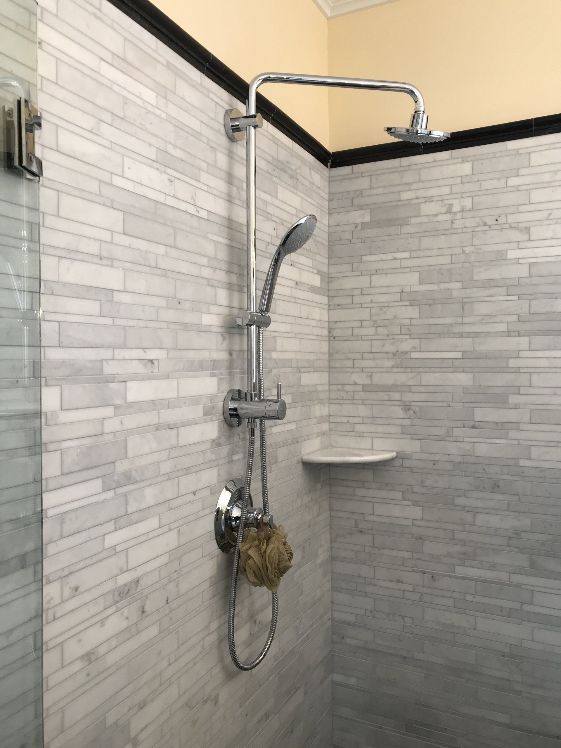 Shower with a handheld showerhead and overhead rain shower on a gray and white tiled wall.