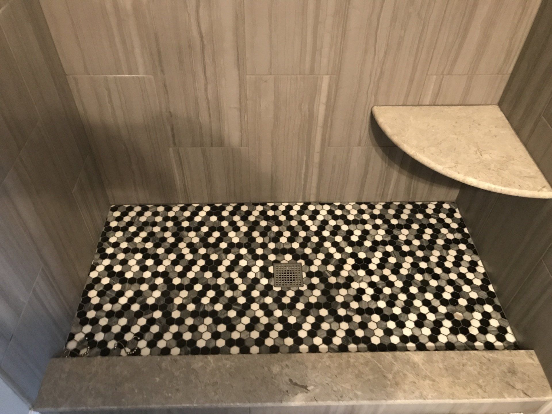 Shower stall with gray walls, black and white hexagon tile floor, and a corner shelf.