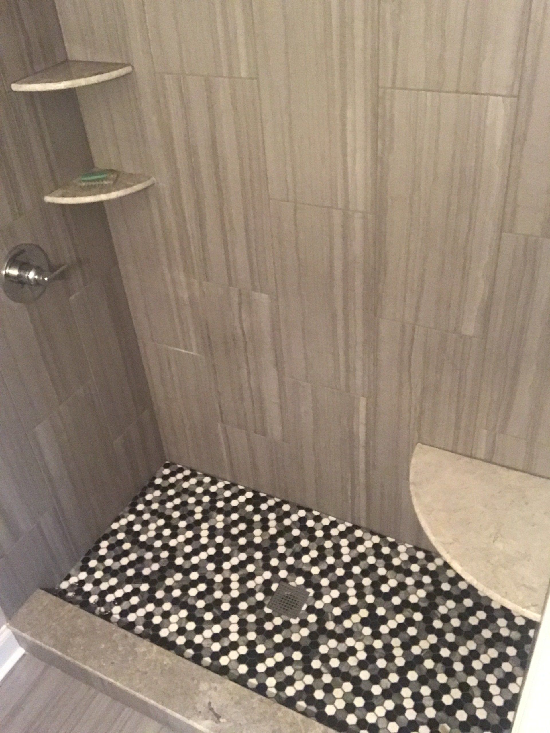 Gray tiled shower with pebble floor and built-in shelves.