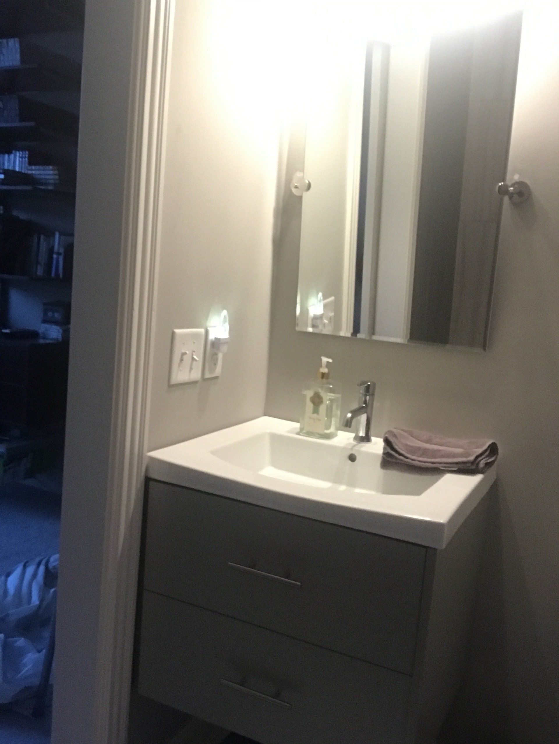 Gray bathroom vanity with mirror, faucet, soap, towel, and a night light in a corner.