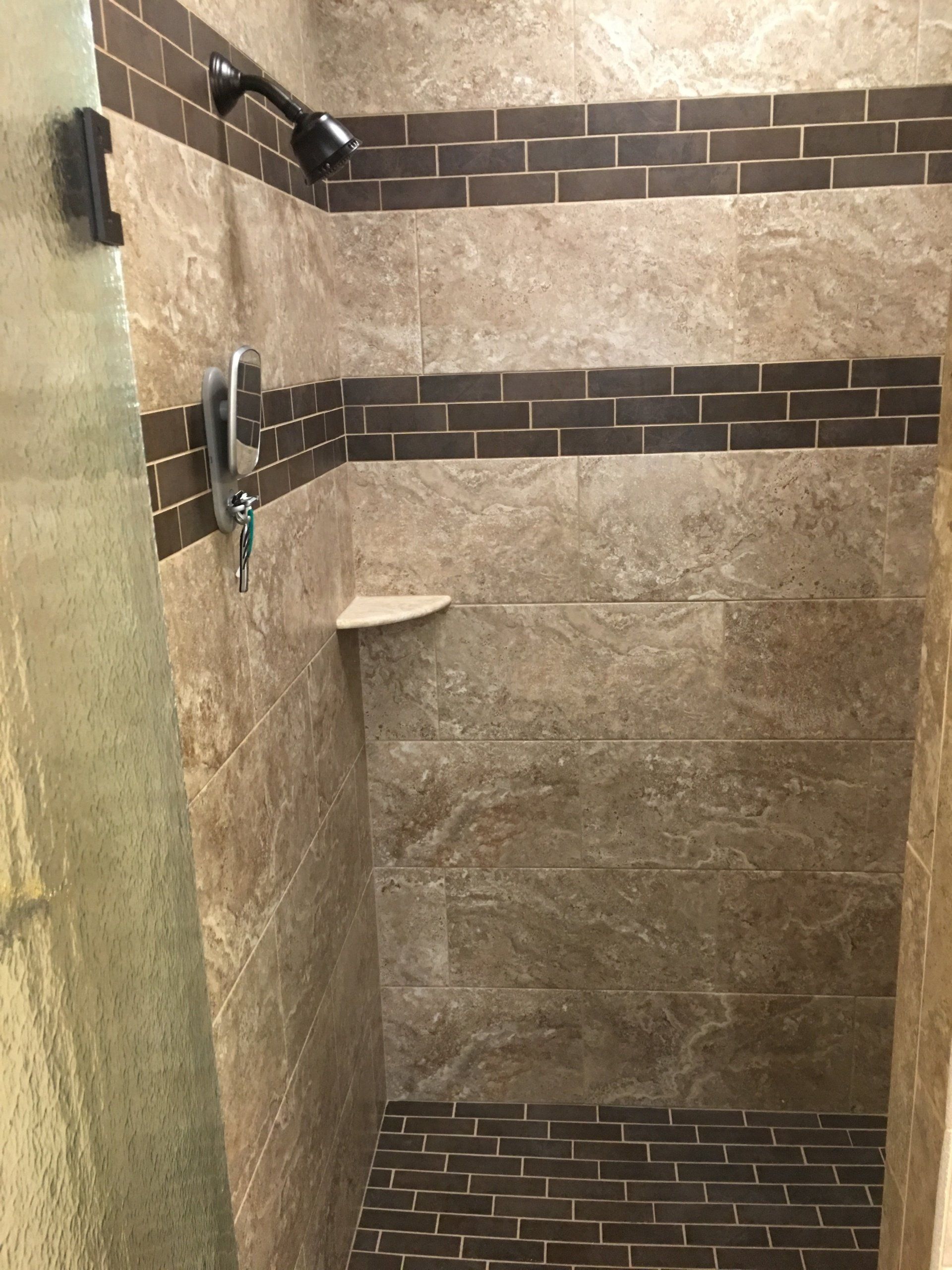 Tiled shower stall with dark brown and tan tiles, including a shelf and showerhead.
