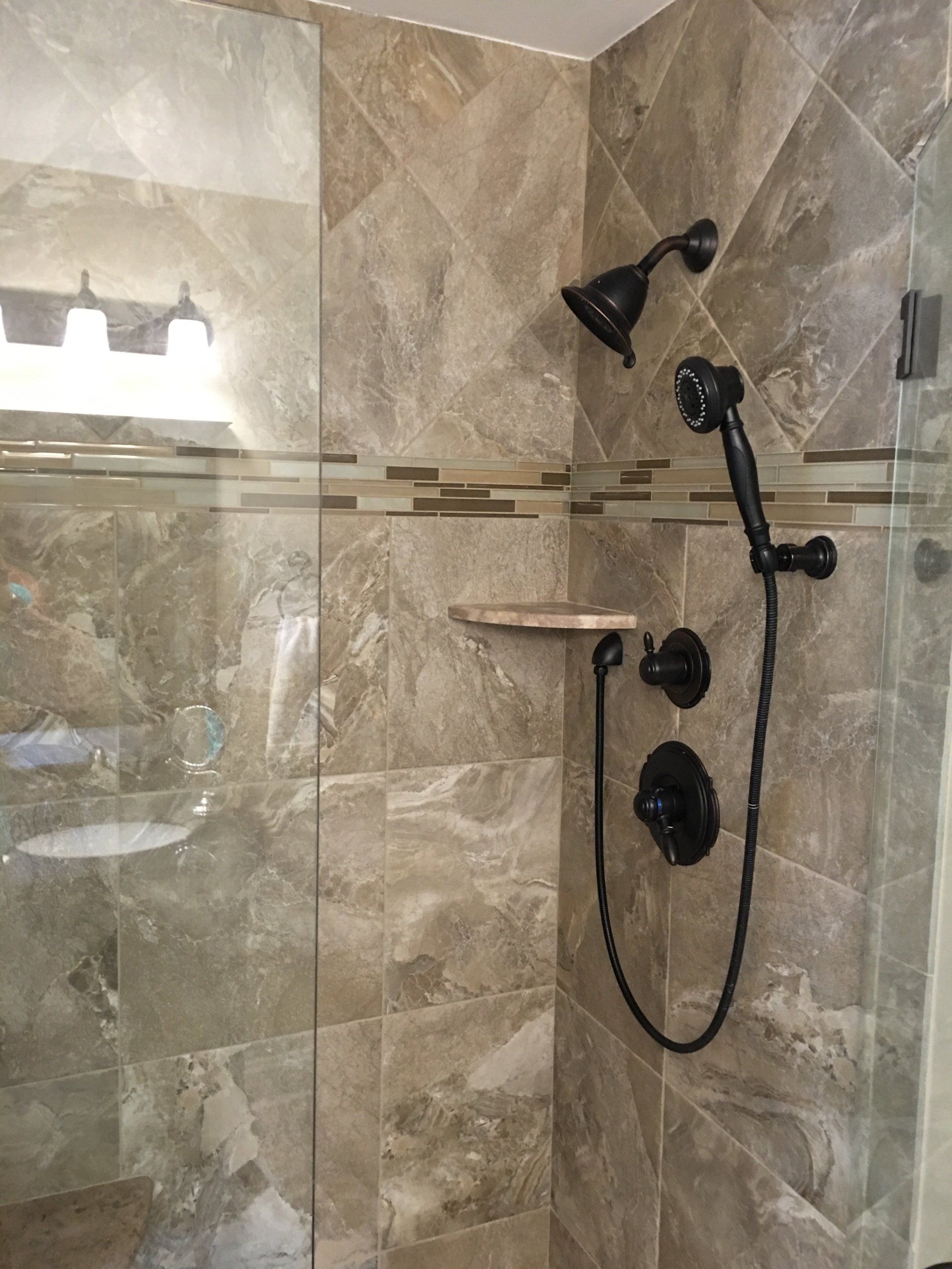 Shower with brown tile, black shower fixtures, and glass door.