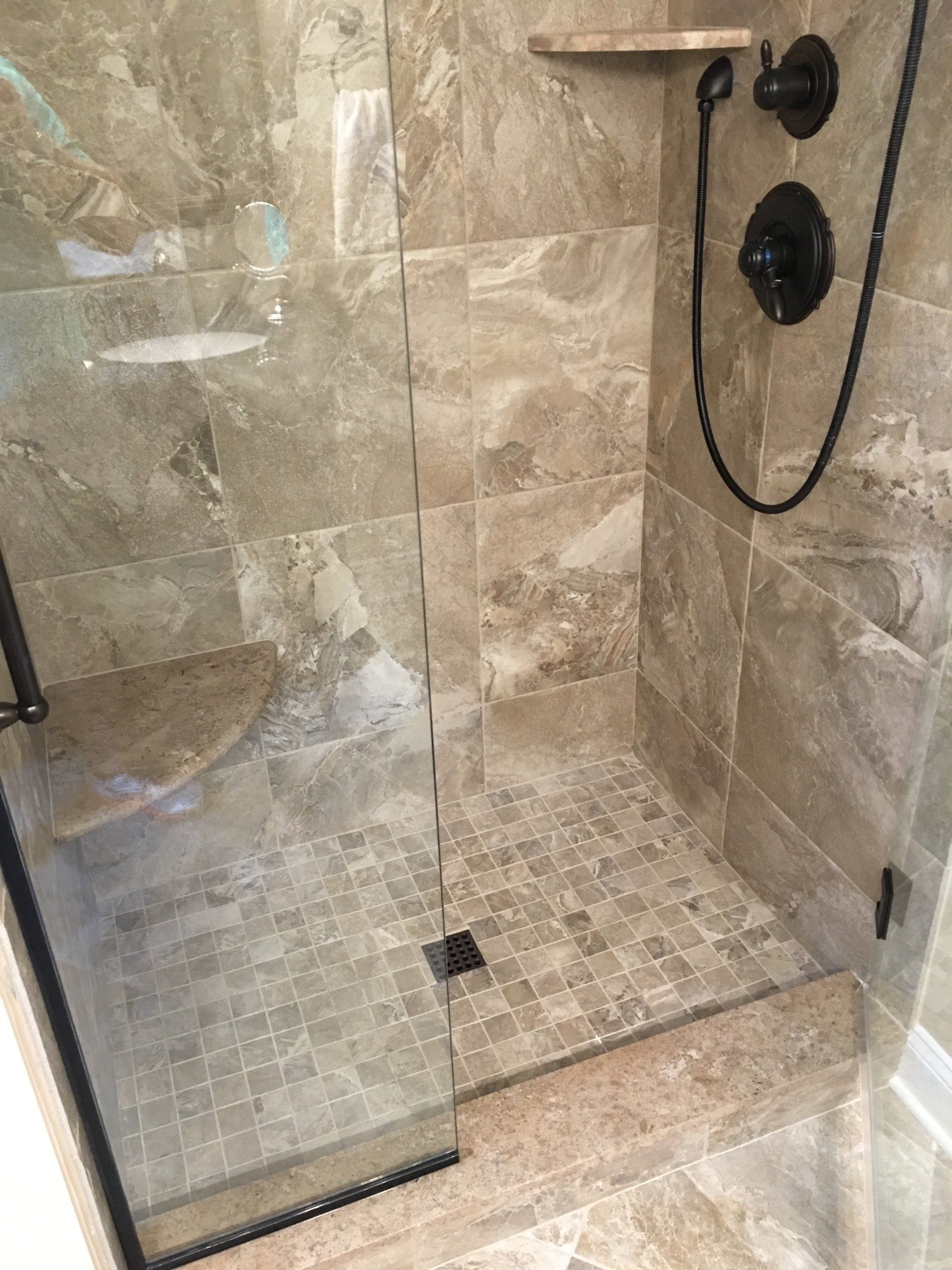 Tiled shower with glass door. Beige tiles on walls and floor, black fixtures.