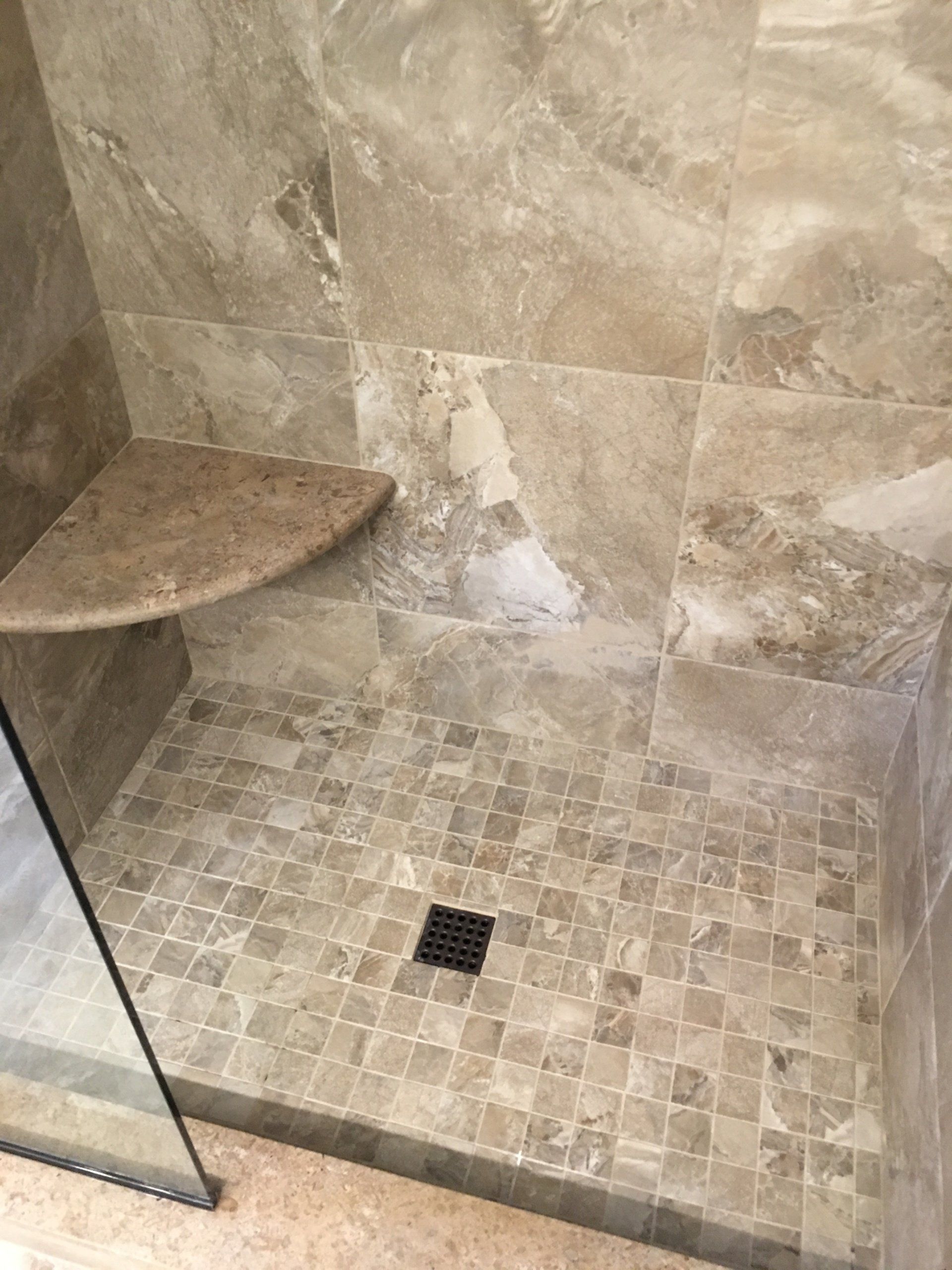 Shower stall with brown tile walls and floor, corner shelf, and black drain.