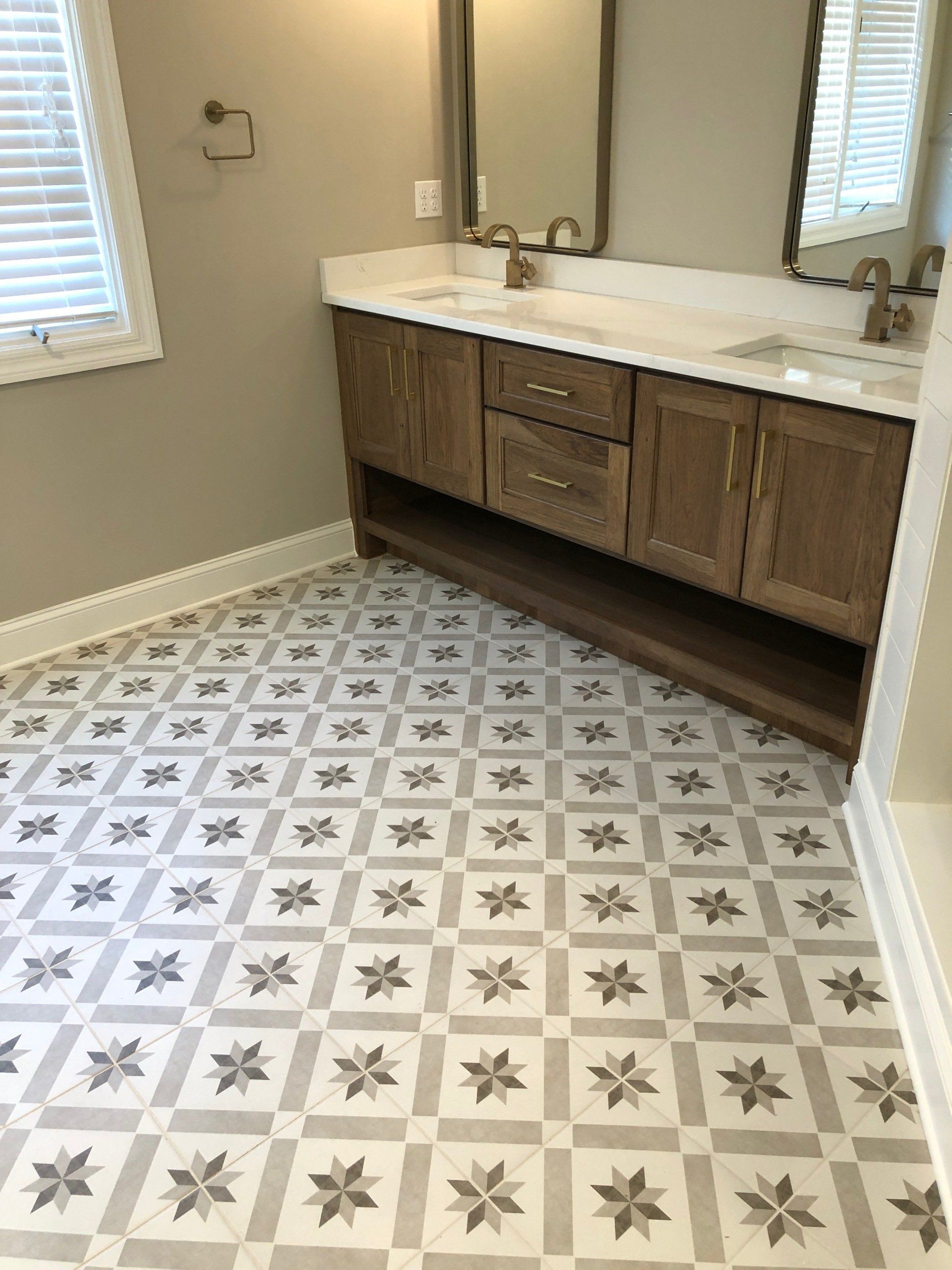 Bathroom with patterned gray and white tile floor, wooden vanity, and a large mirror.