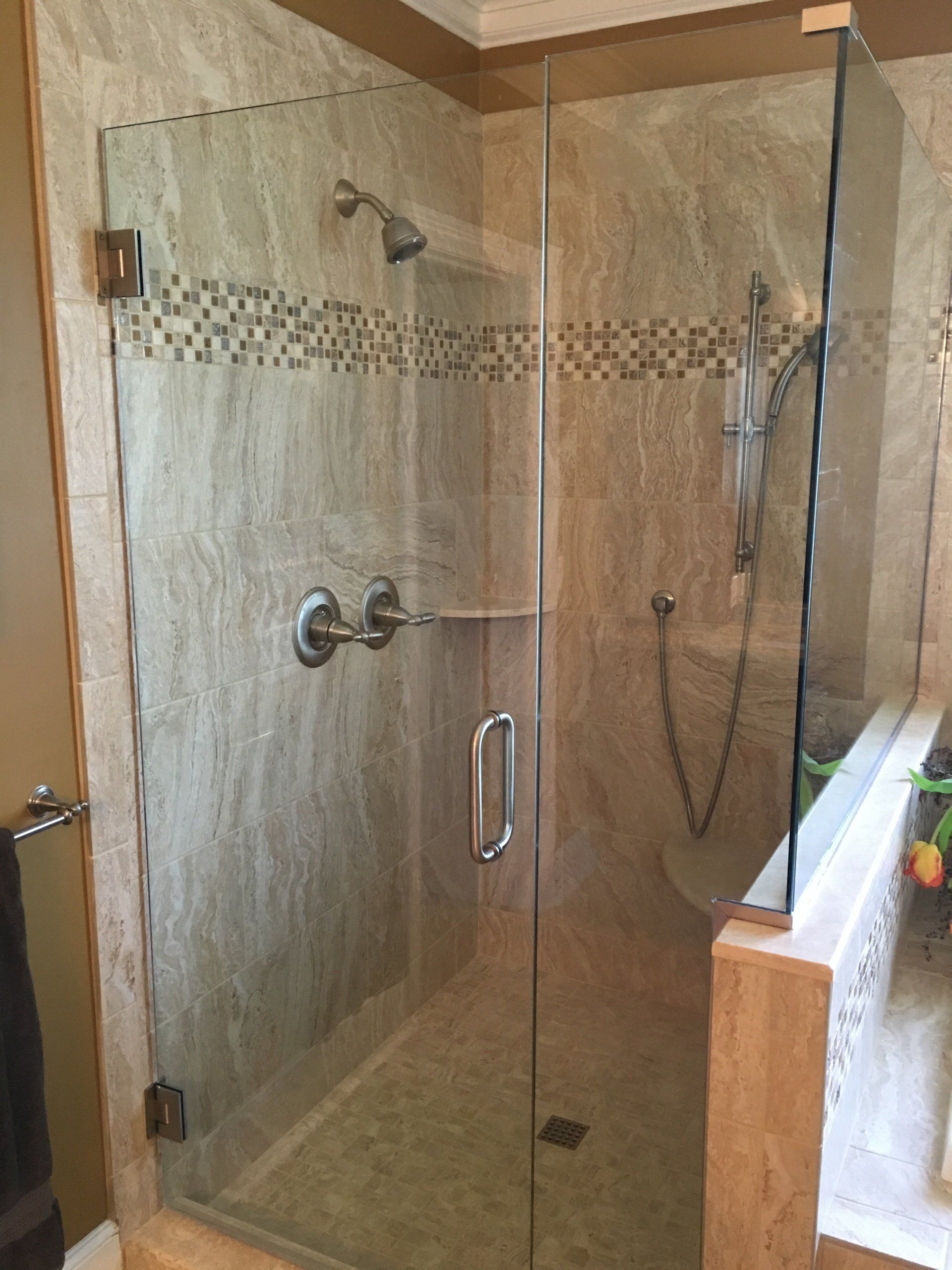 A modern bathroom shower with a clear glass door, beige tile, and silver fixtures.