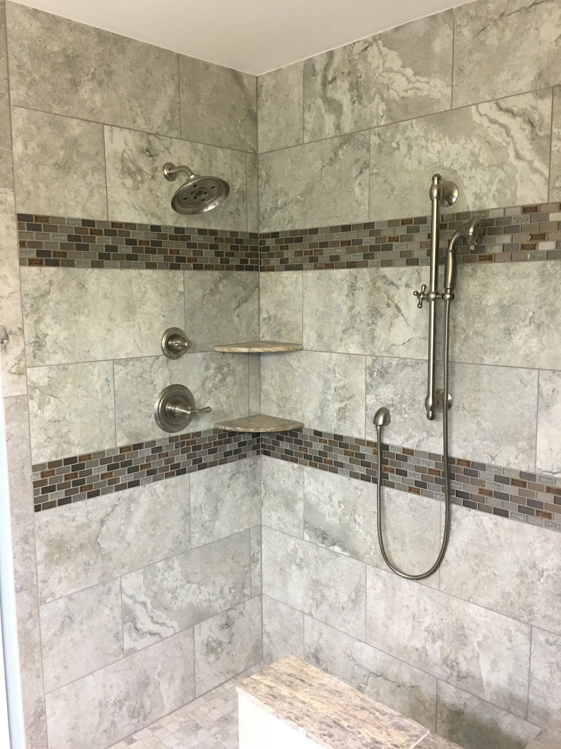 Shower with gray tiles, mosaic band, and silver fixtures. Includes a bench and two shelves.