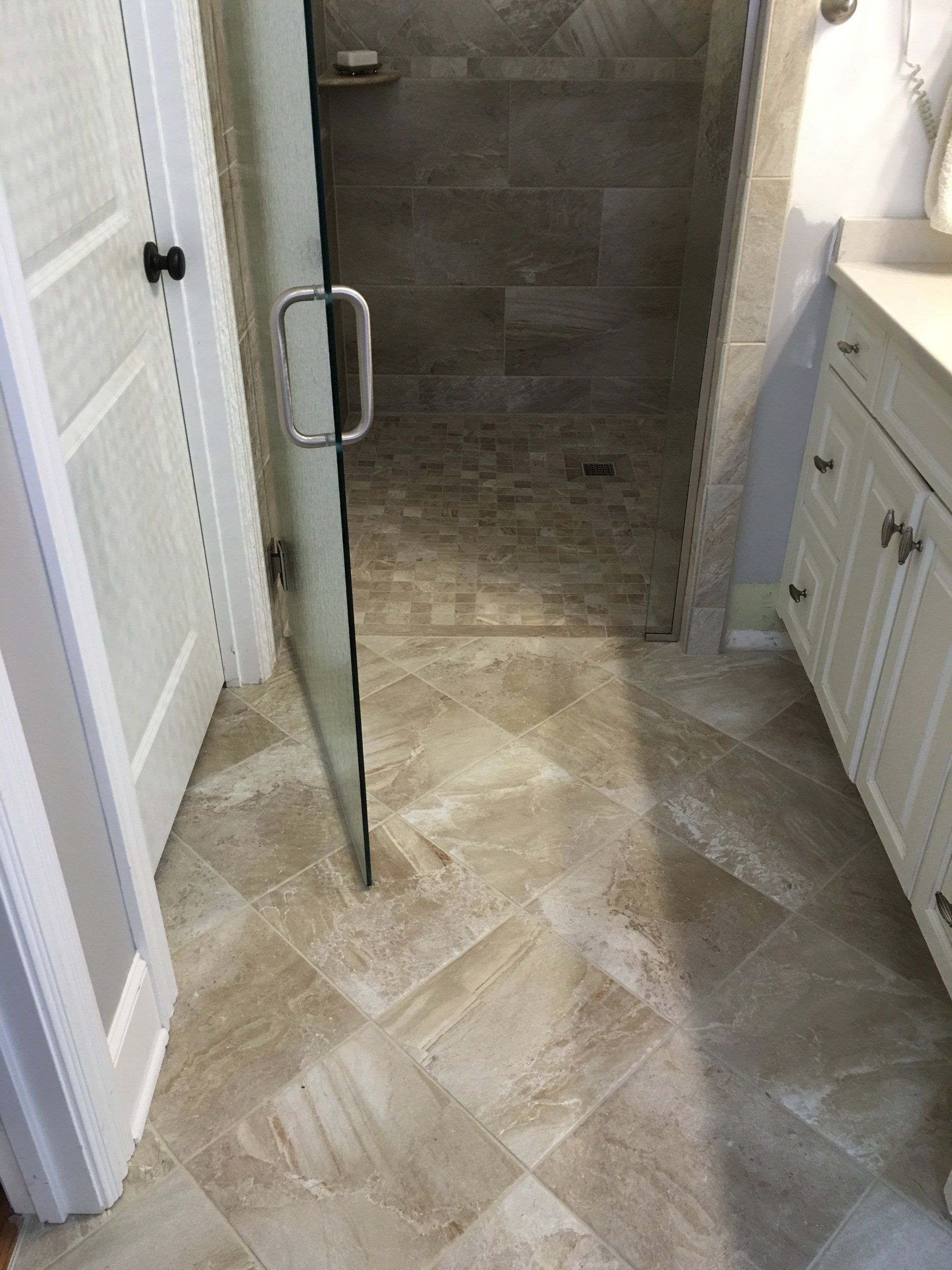 Bathroom with tile floor, shower with glass door, white cabinets.