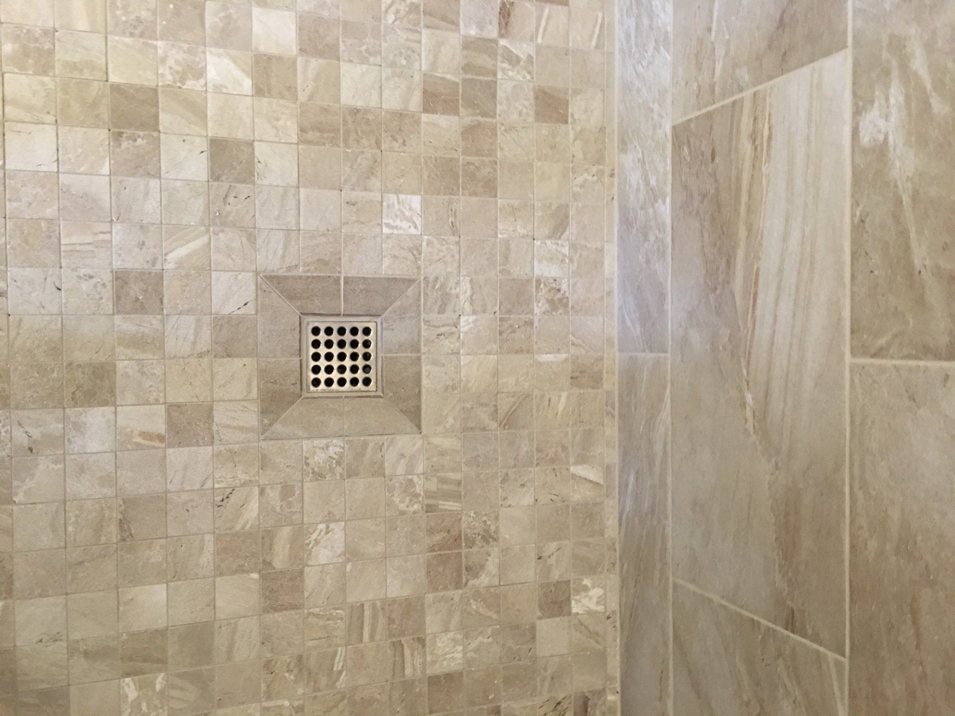 Tan tile shower with square floor drain and large, smooth wall tiles.