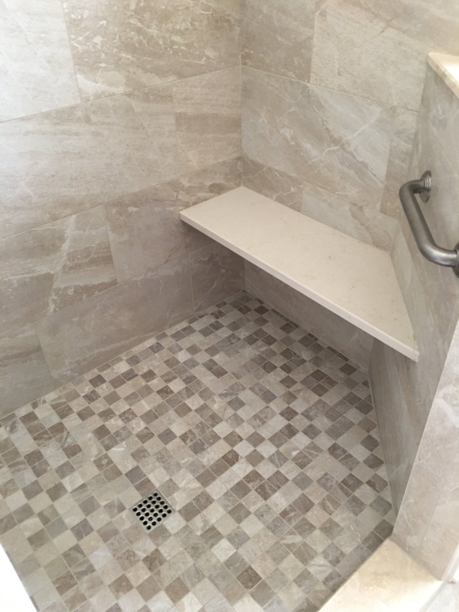 Shower stall with a built-in corner seat, grab bar, and patterned tile floor.