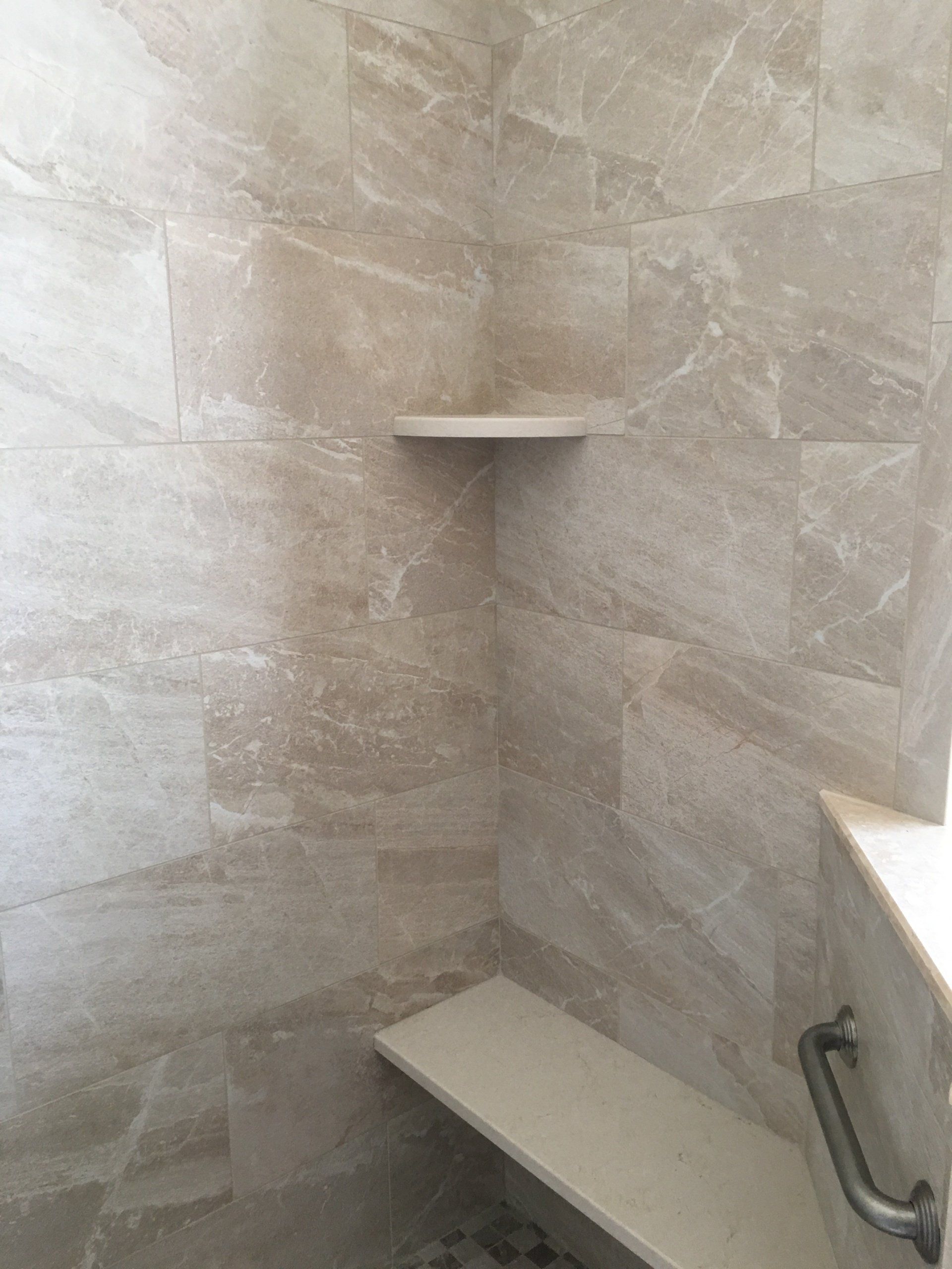 Tiled shower with a built-in bench and shelf, a handrail, and neutral color tones.