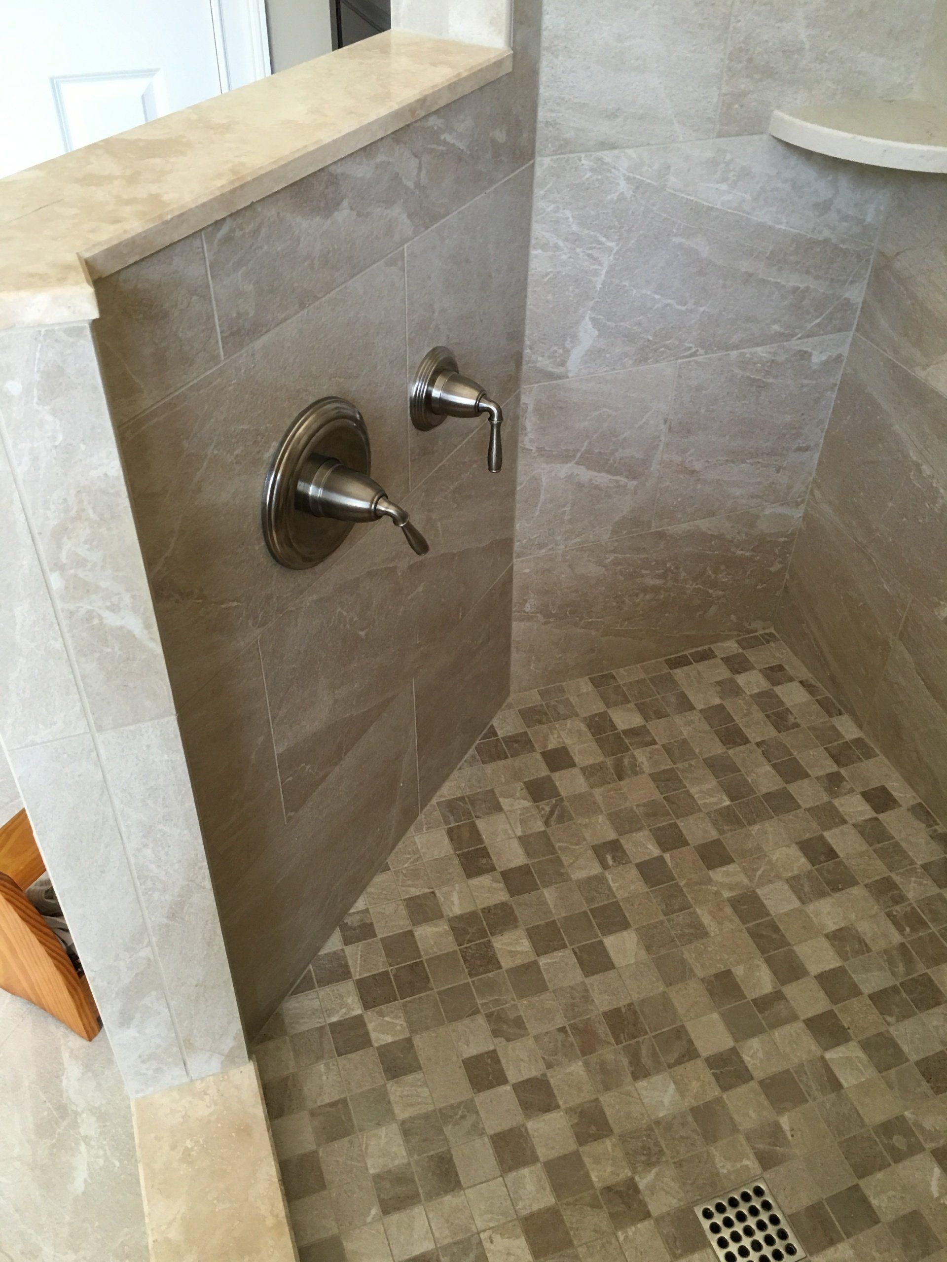 Shower with beige tile walls and mosaic floor; bronze faucet fixtures.