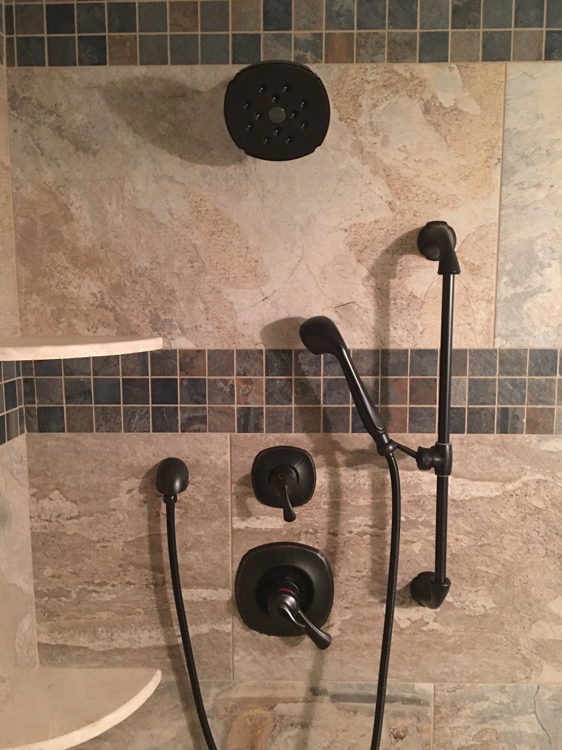 Shower with black fixtures, including a showerhead, handheld shower, and control knobs, set against tile.