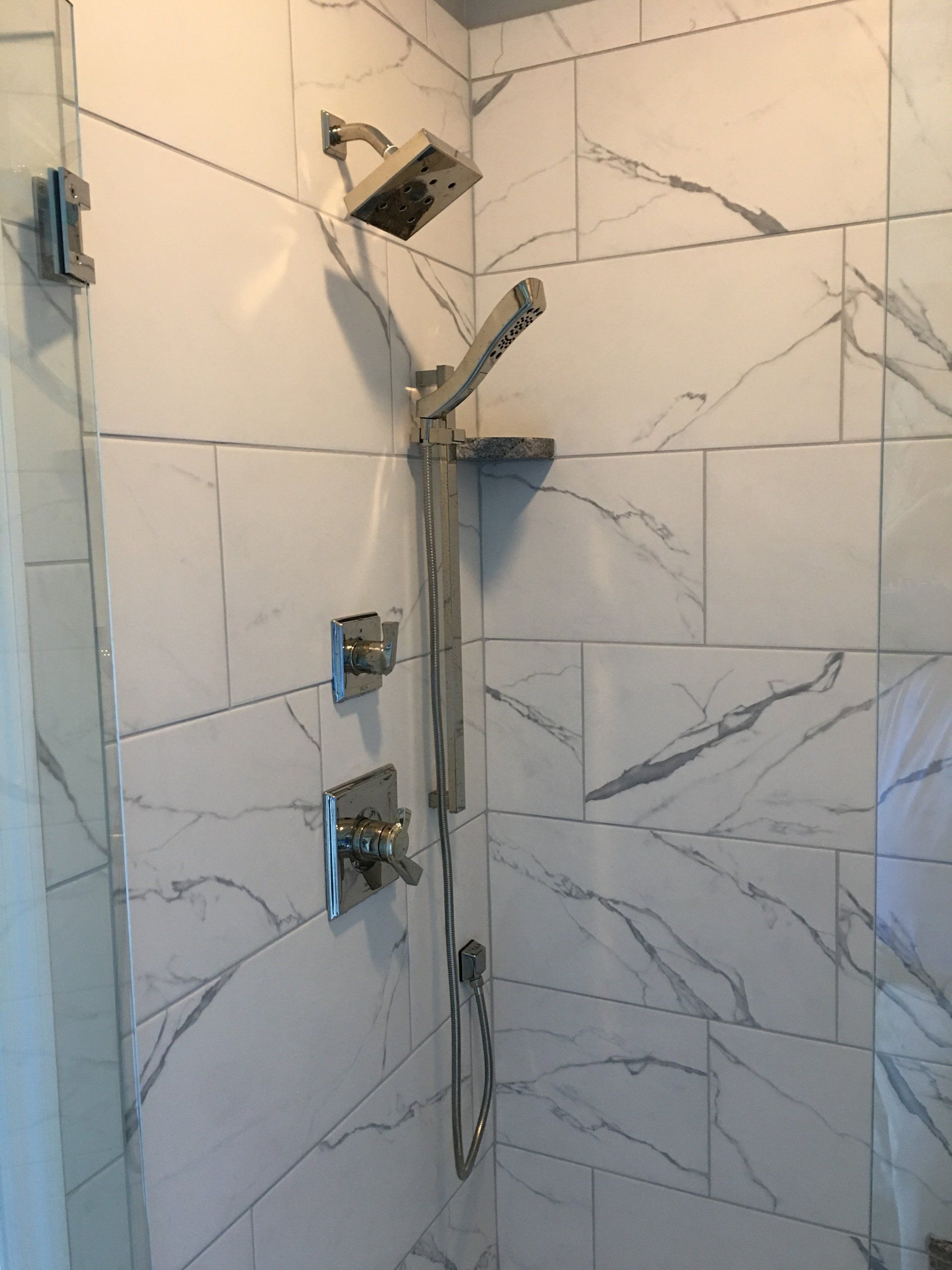 Shower with white marble-look tiles and silver fixtures, including a rain shower head and handheld wand.