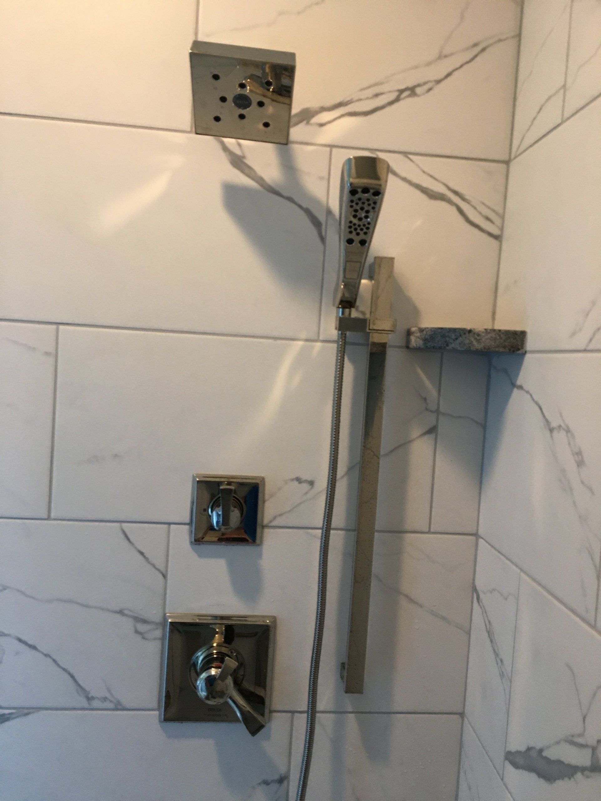 Shower with silver fixtures on marble-like tile.