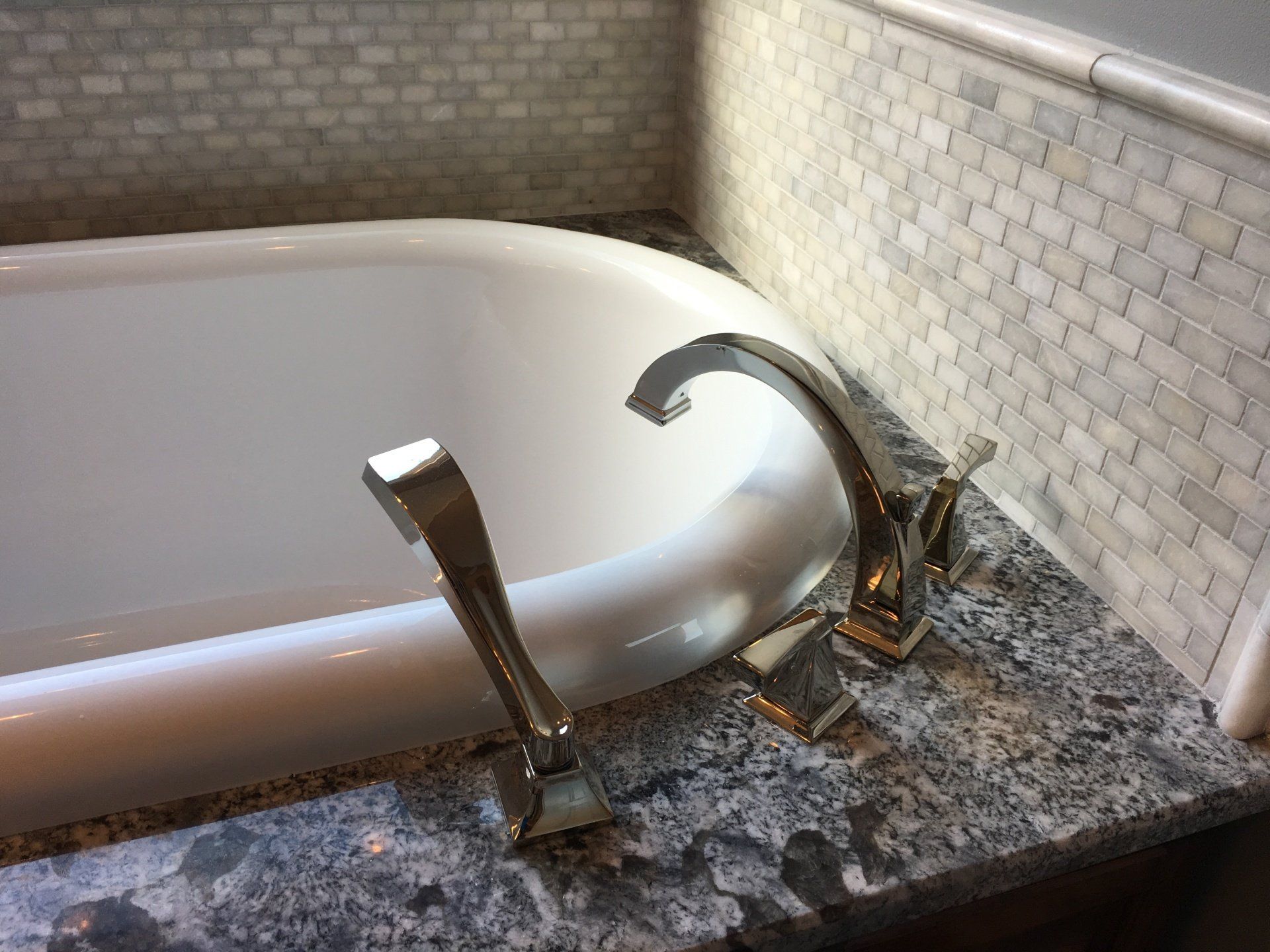 Clawfoot bathtub with silver faucet, on a speckled granite countertop. Tile wall in the background.