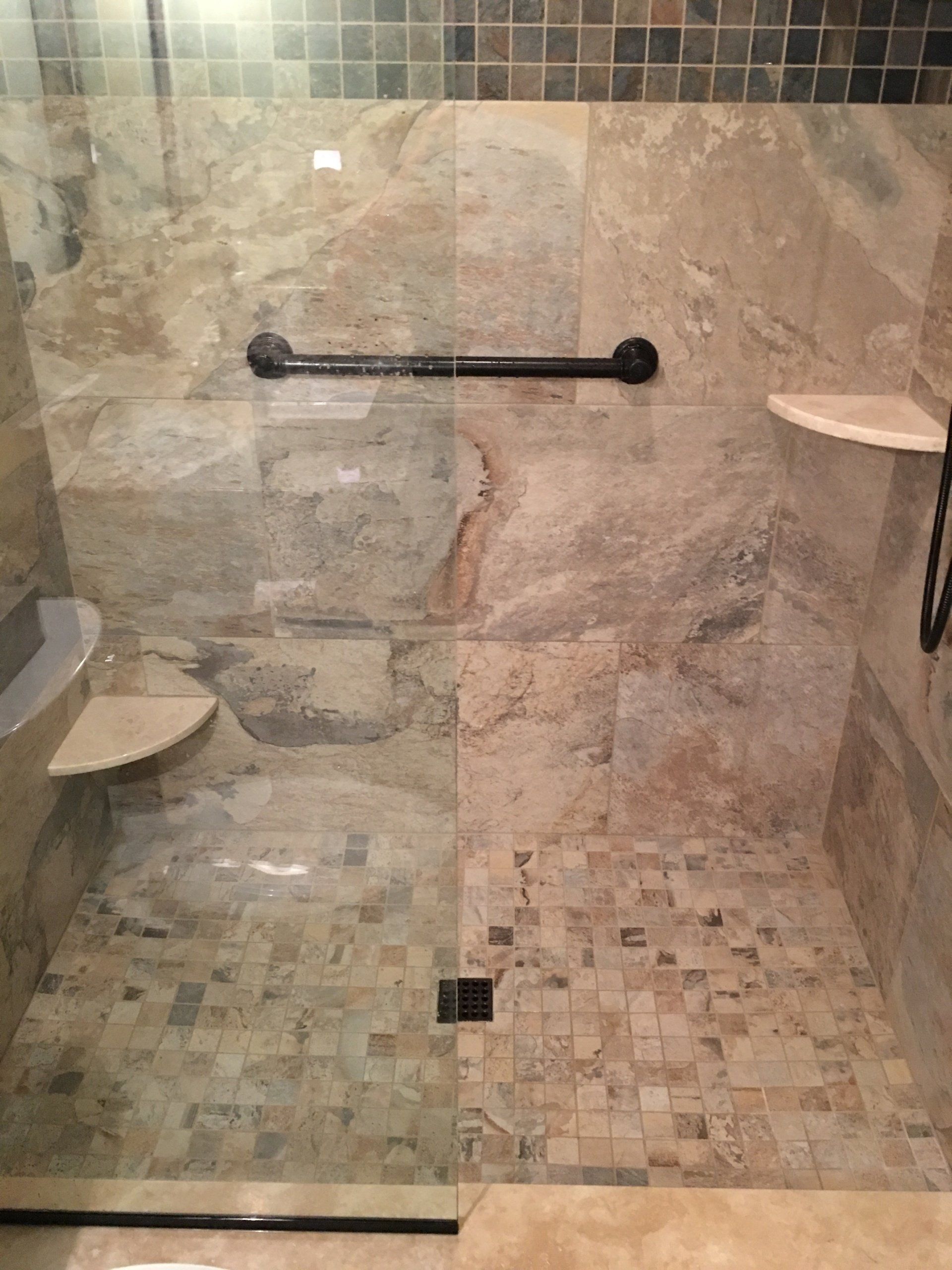 Shower with stone walls, glass door, grab bar, and small mosaic tile floor.