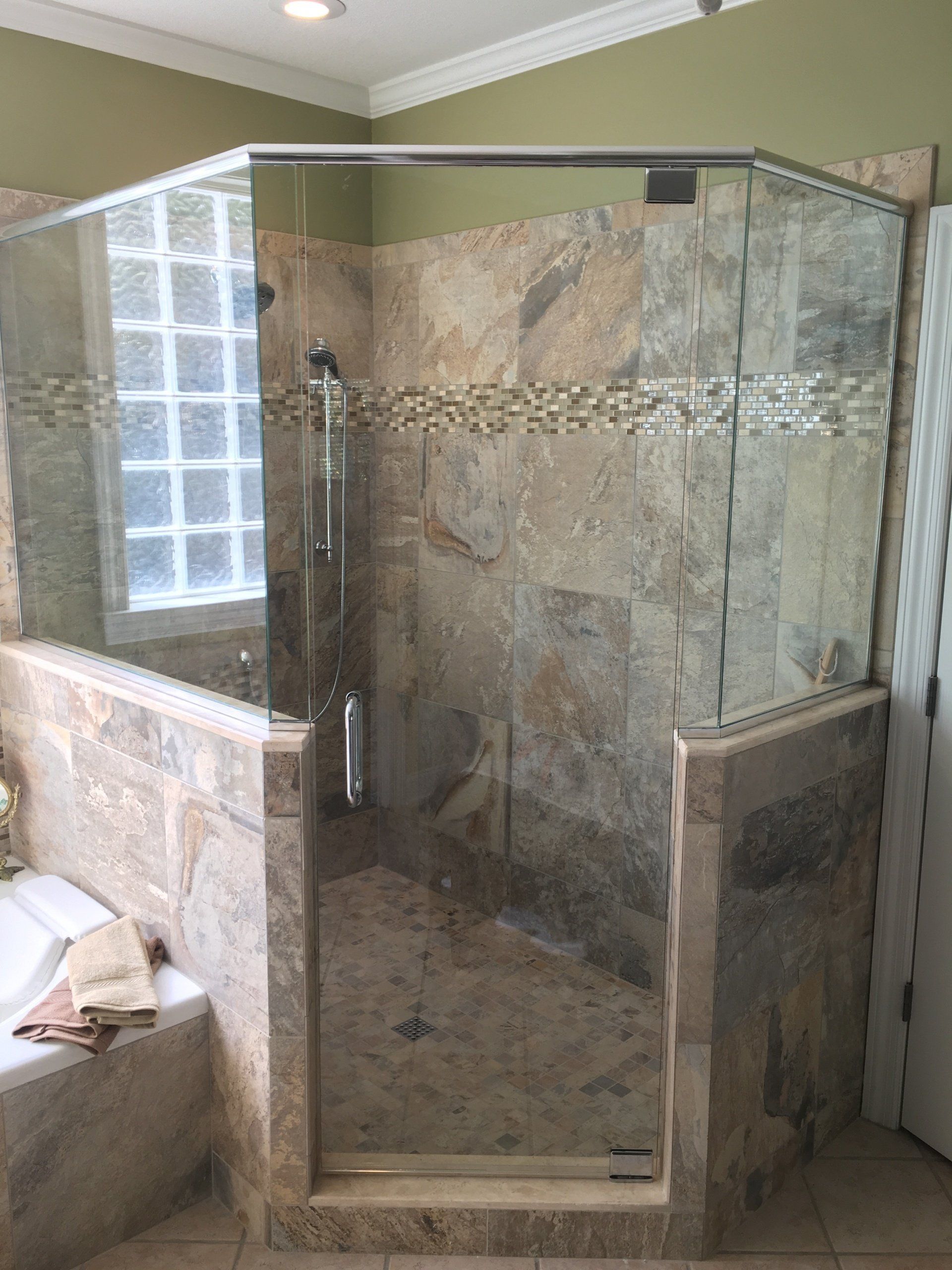 A tiled shower with a glass enclosure and a walk-in entrance. Light stone tile is used.