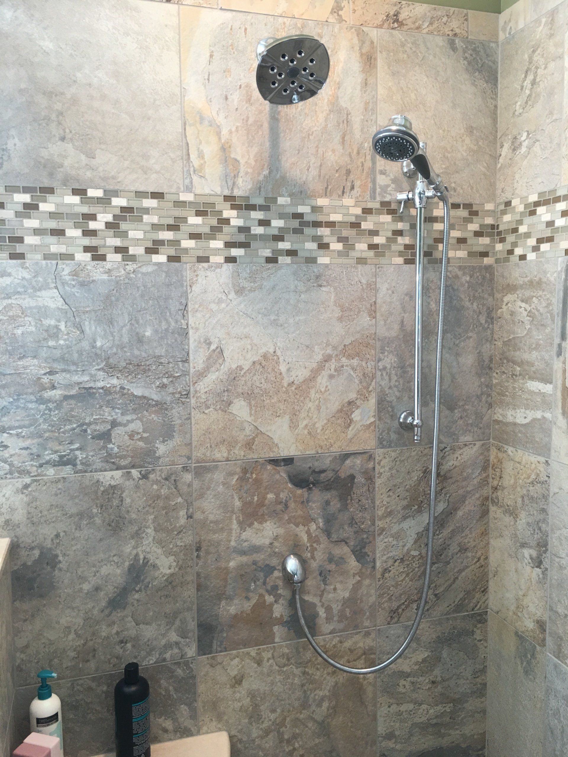 Shower with stone-look tile, dual shower heads, and mosaic tile strip.