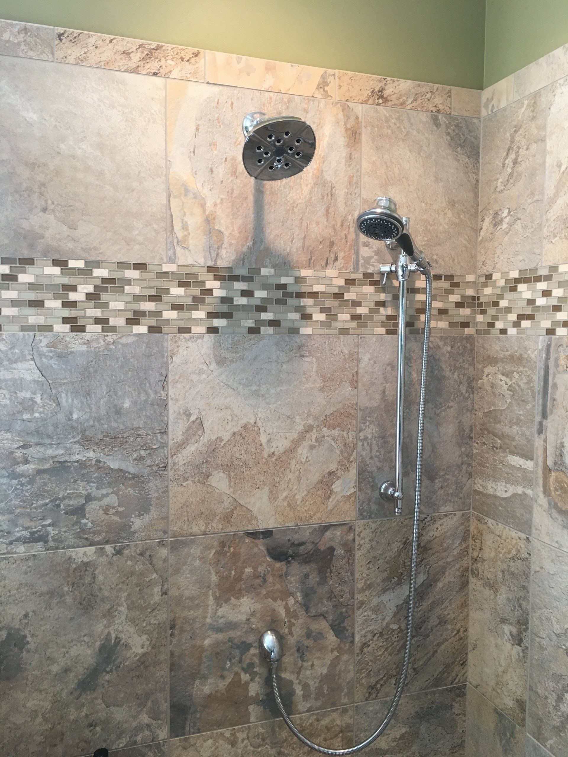 Shower with large stone tiles, a wide showerhead, and a handheld showerhead.