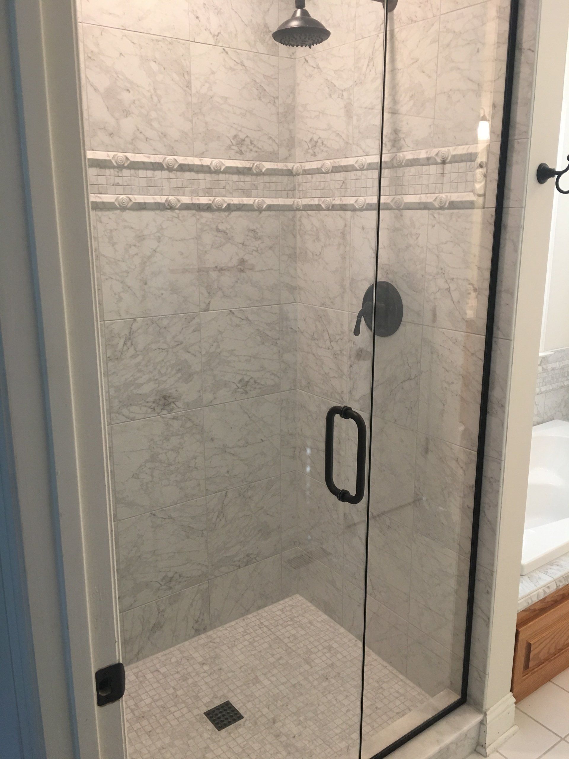 Shower with marble tile walls, glass door, dark hardware.