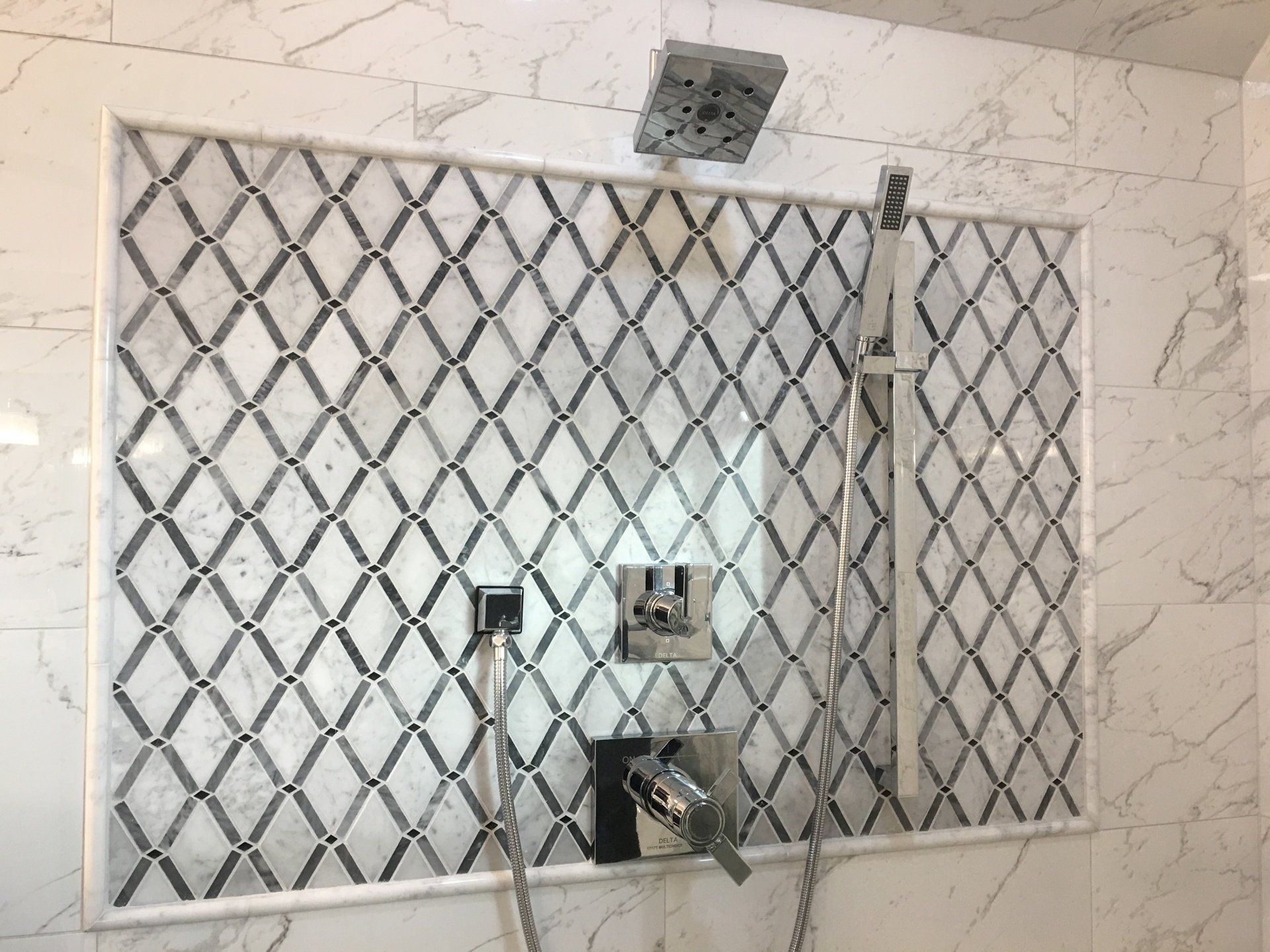 Shower with diamond-patterned mosaic tile, stainless steel fixtures, and a white marble wall.