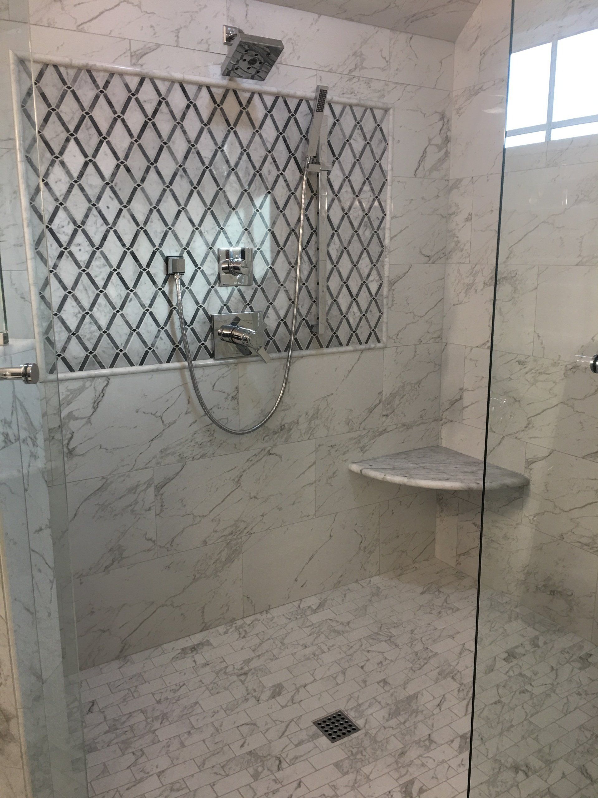 Marble-tiled shower with glass door, bench, and ornate mosaic detail. Chrome fixtures.