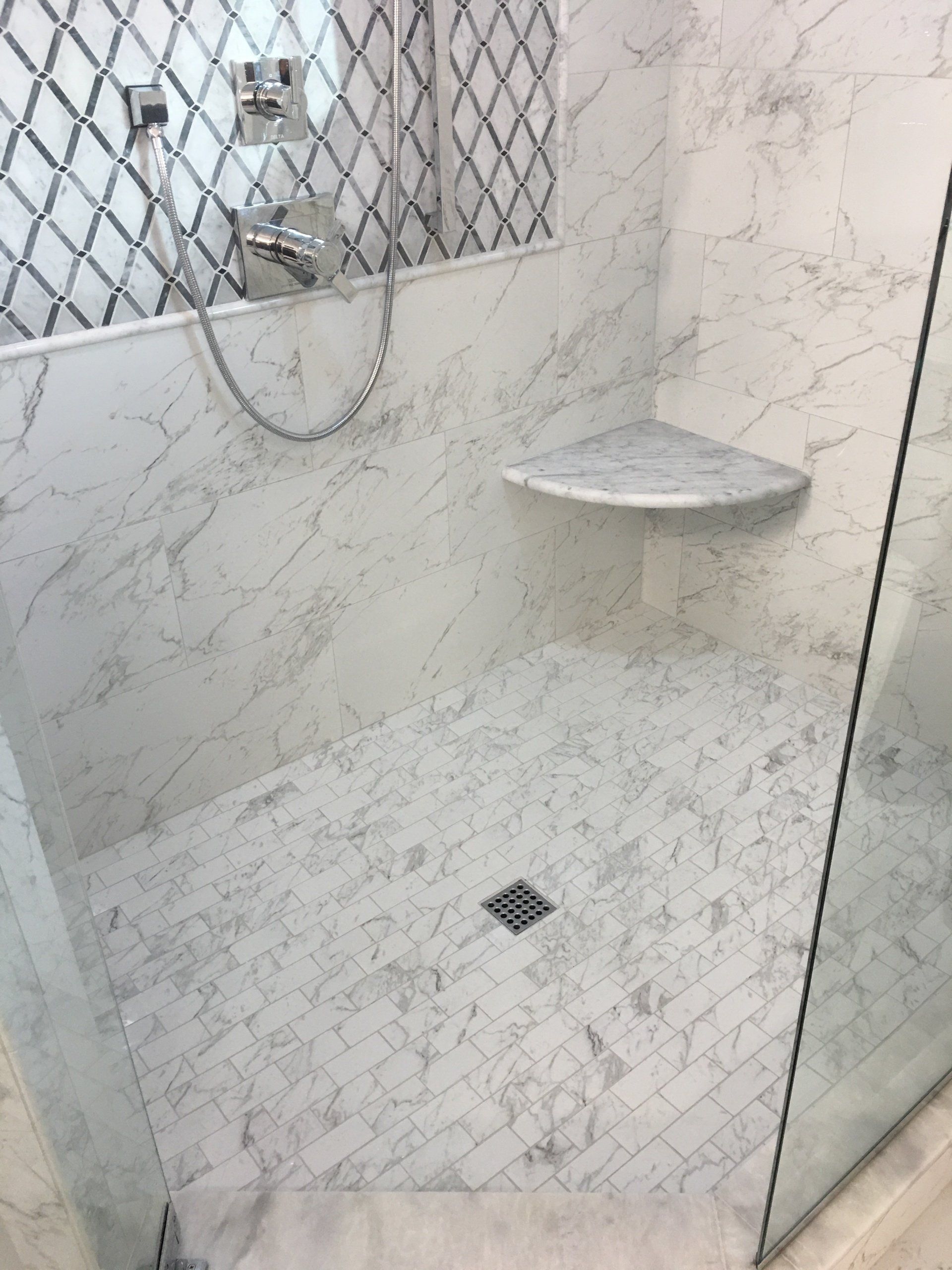 Marble shower with a corner shelf and glass door.