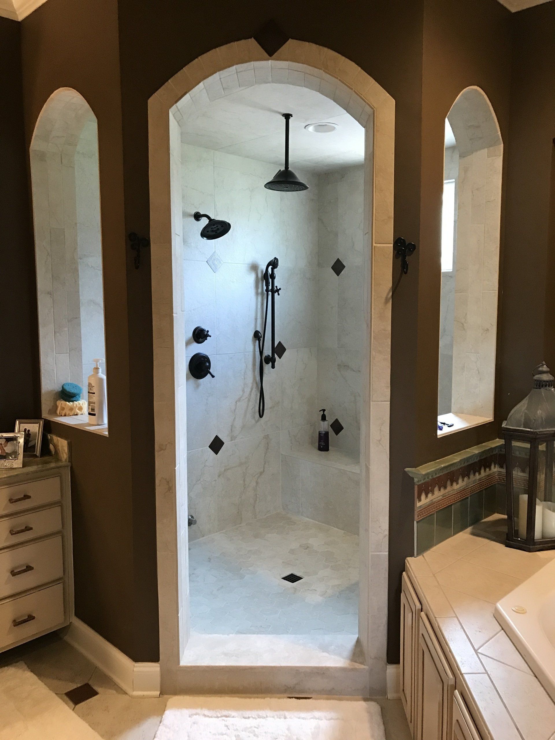 Bathroom with arched shower entrance, brown walls, white tile, black fixtures, and a light-colored cabinet.