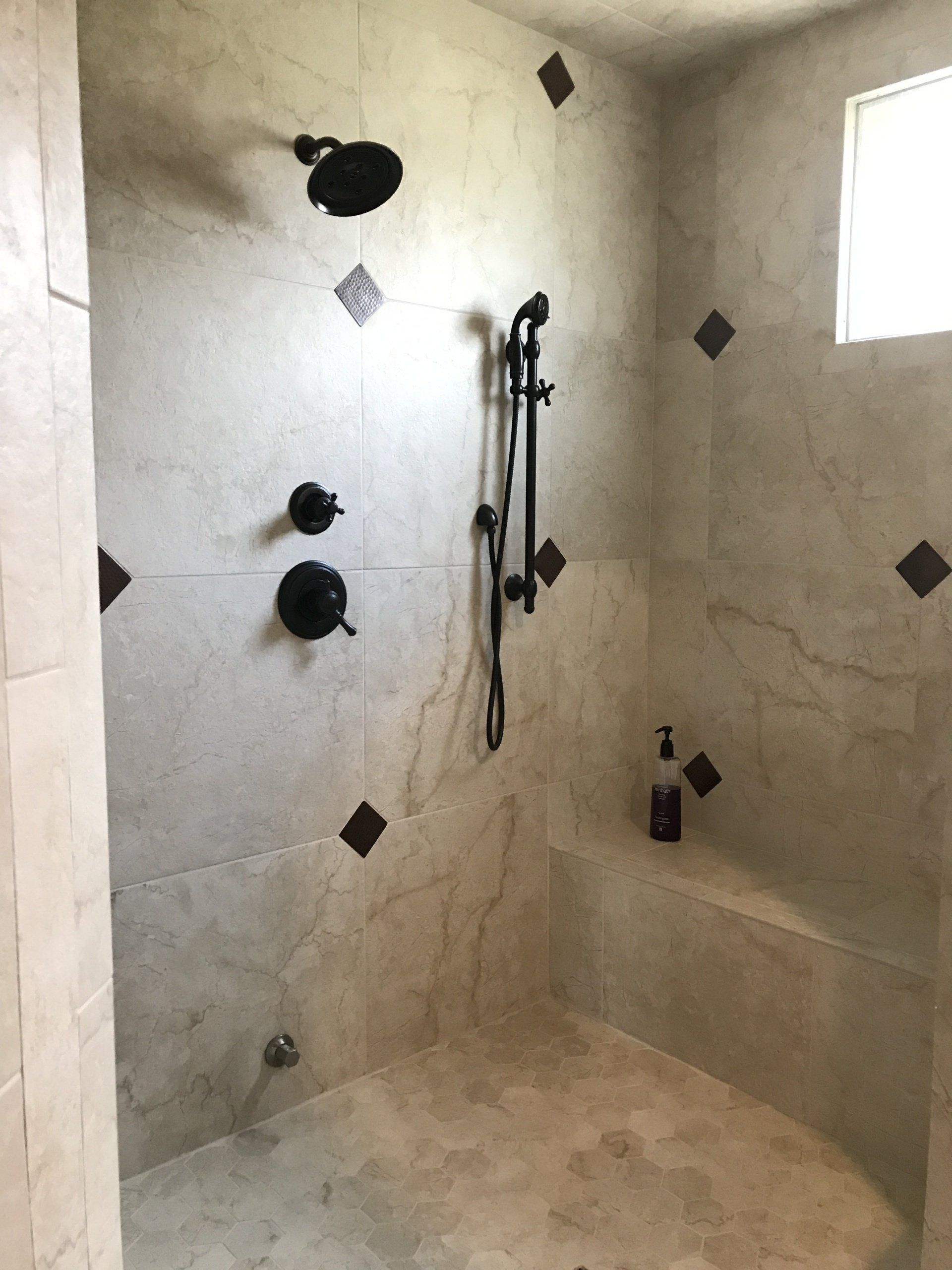A neutral-toned, tiled shower with dark fixtures, brown accent tiles, and a built-in bench.