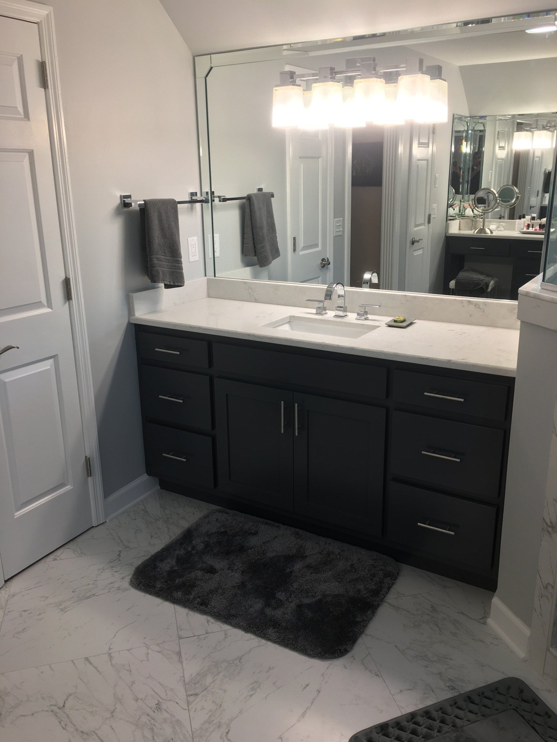 Bathroom with a dark gray vanity, white countertop, large mirror, and gray rug.