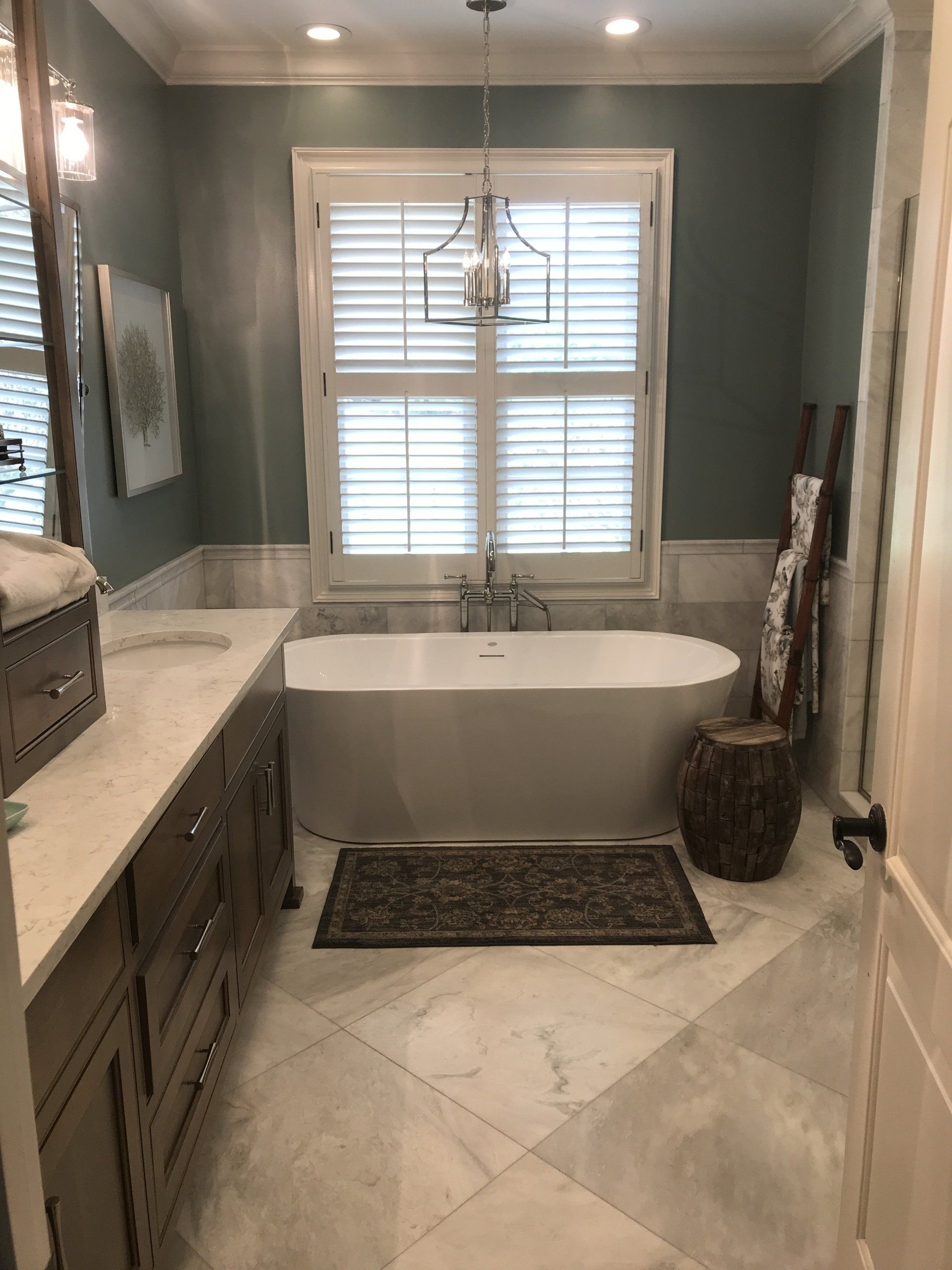 Bathroom with white tub, shutters, blue wall, and a wooden ladder.