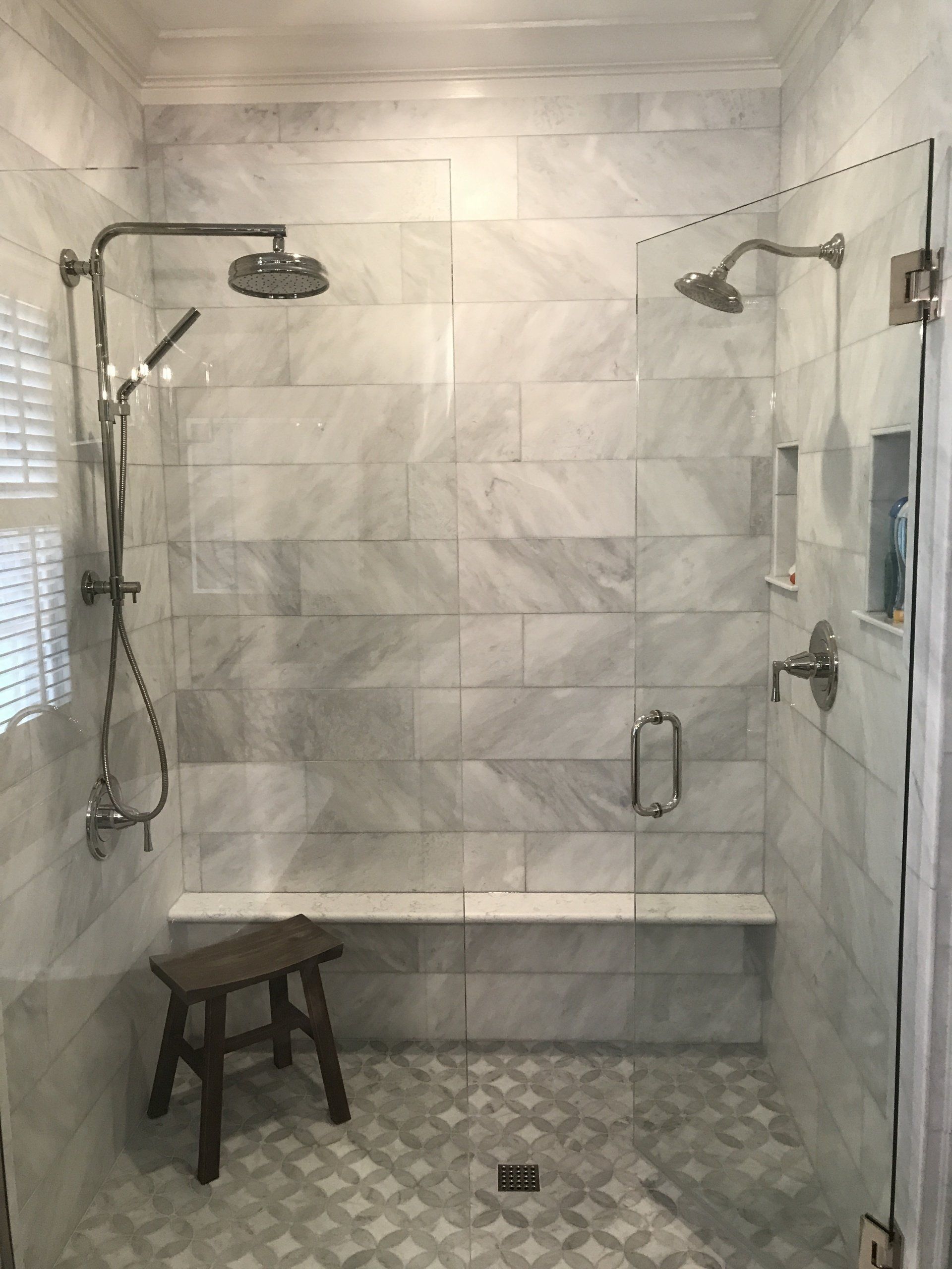 Marble-tiled shower with glass doors, two showerheads, a built-in bench, and a small wooden stool.