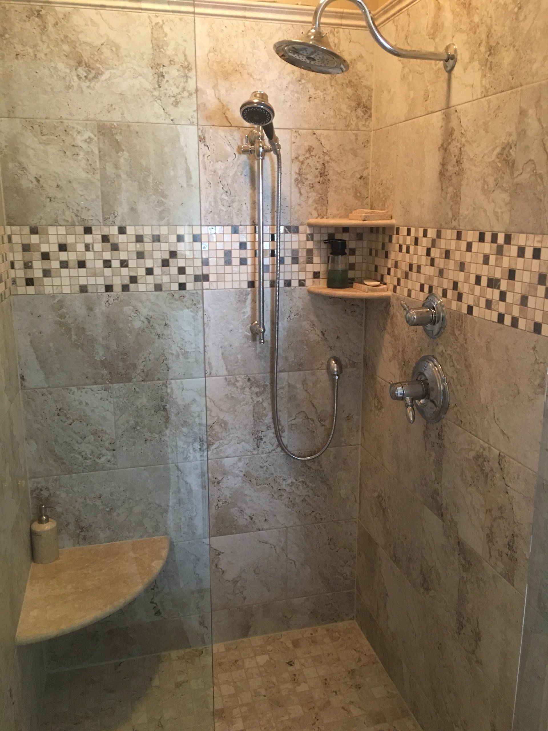 Shower stall with beige tiled walls, built-in shelves, and silver shower fixtures.