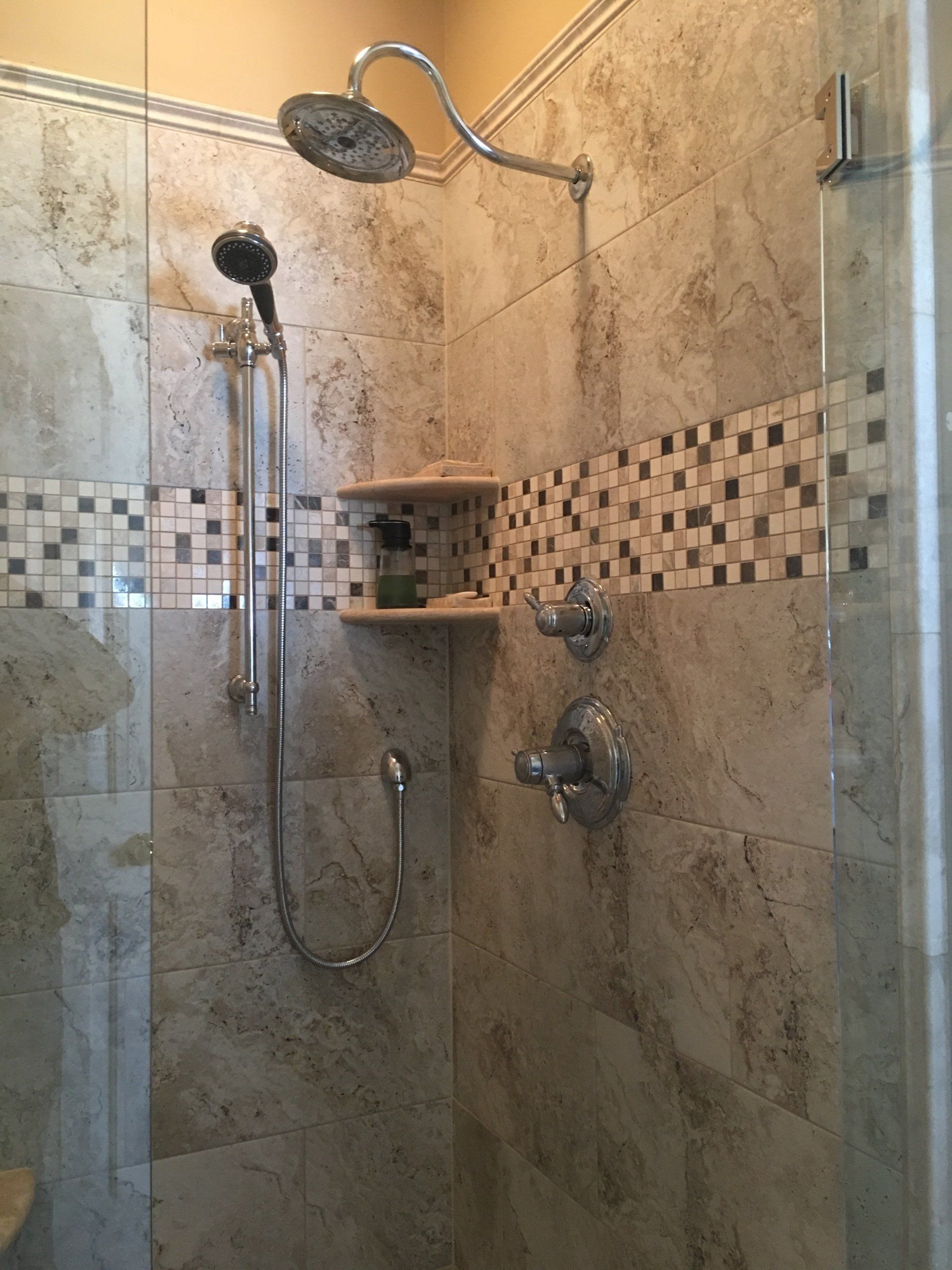Shower with stone tiles, mosaic accent, glass door, and handheld showerhead.