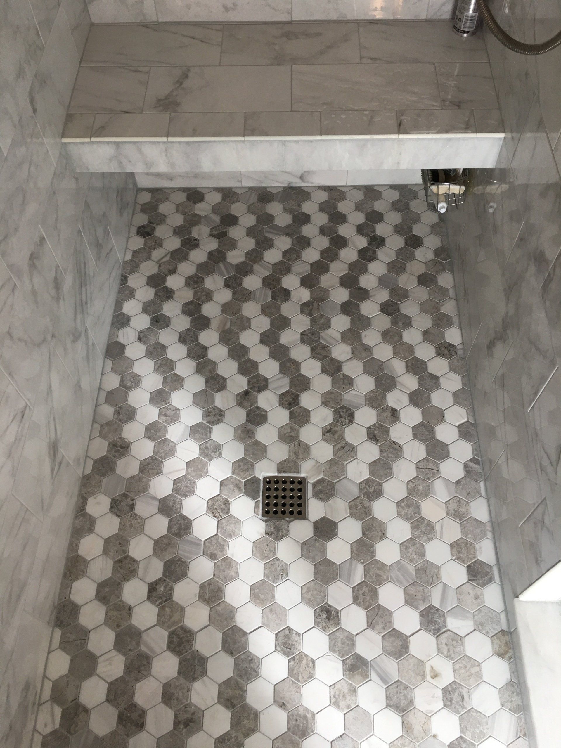 Shower with patterned grey and white honeycomb tiles, drain in center.