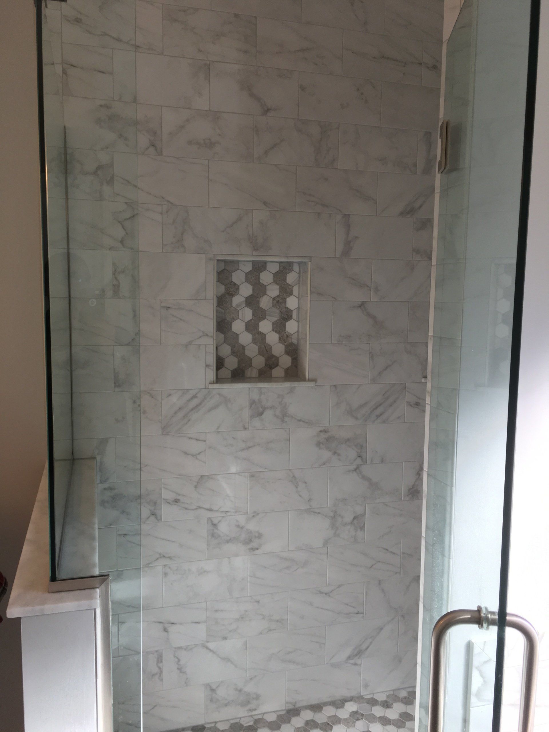 Shower with marble tile walls and a decorative niche. A glass door is on the right side.