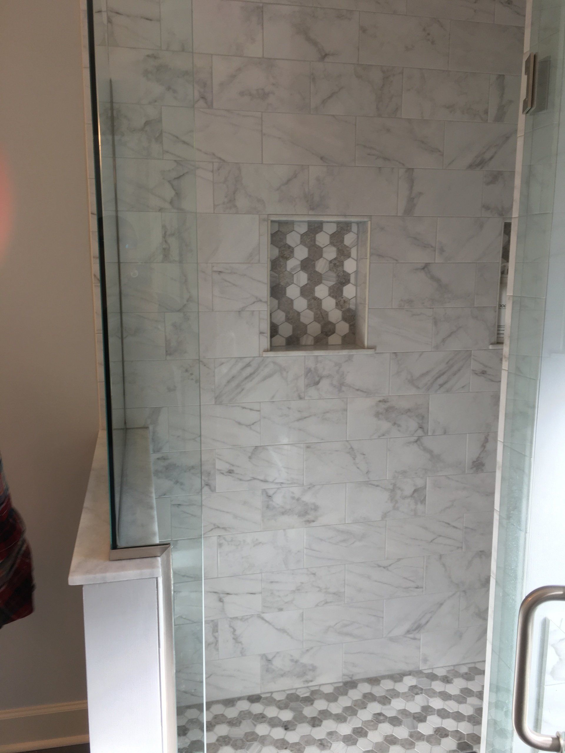 Shower with marble tile walls, glass door, and small niche with decorative tile.