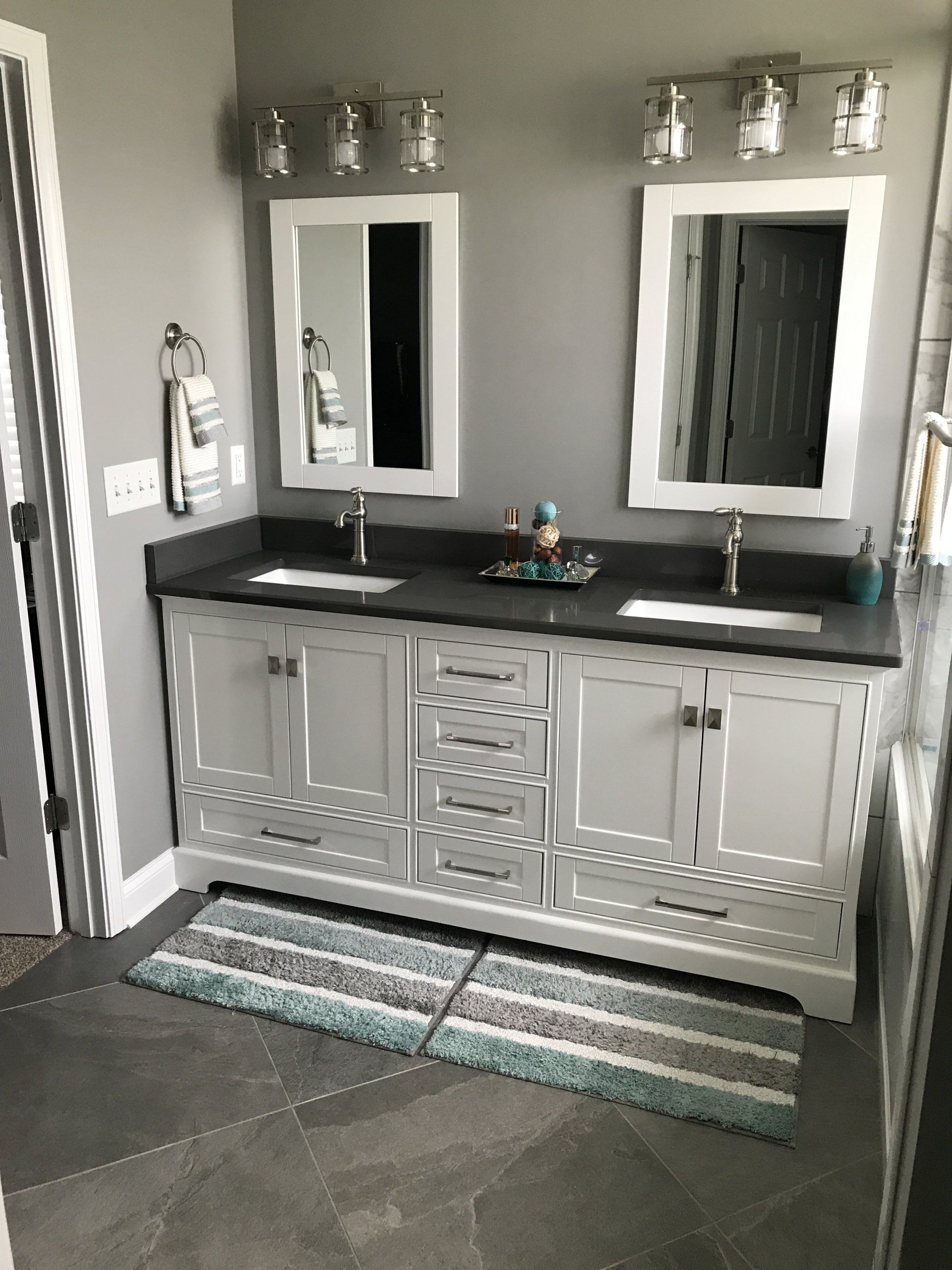A bathroom with a white double vanity, two mirrors, gray walls, and a blue and gray rug.