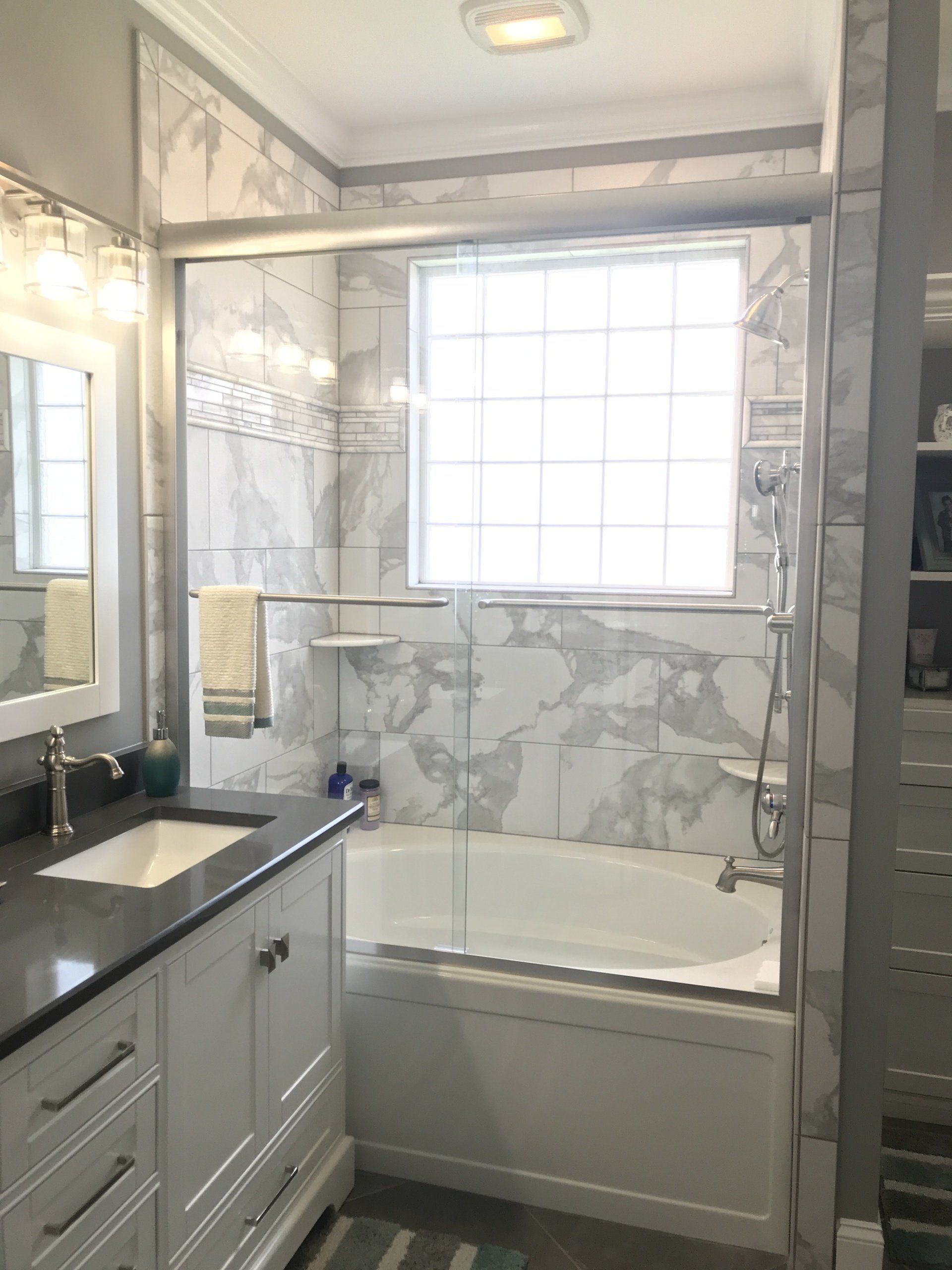 Bathroom with white vanity, tub, and marble tile. Window in shower area.